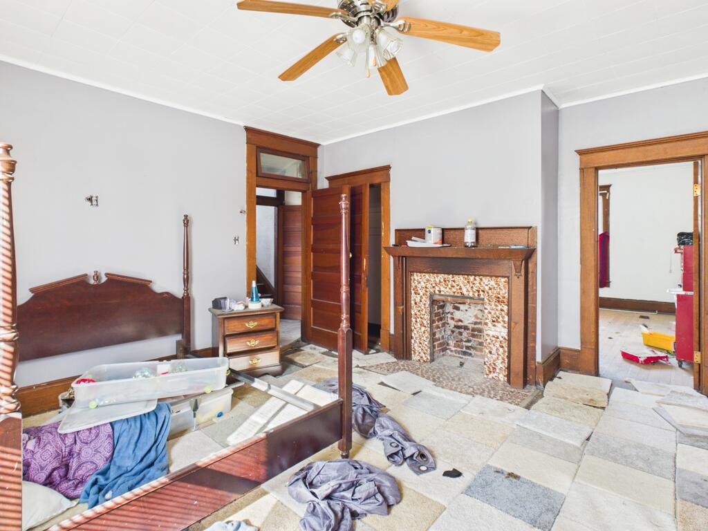 Bedroom with an exposed-brick fireplace, dark wood trim, and a partially dismantled bed amid renovation debris.