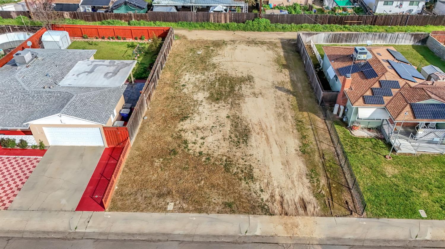 Aerial view of a vacant fenced residential lot between neighboring homes.