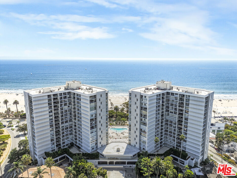 Two beachfront condominium towers overlook the ocean, with a pool between them.