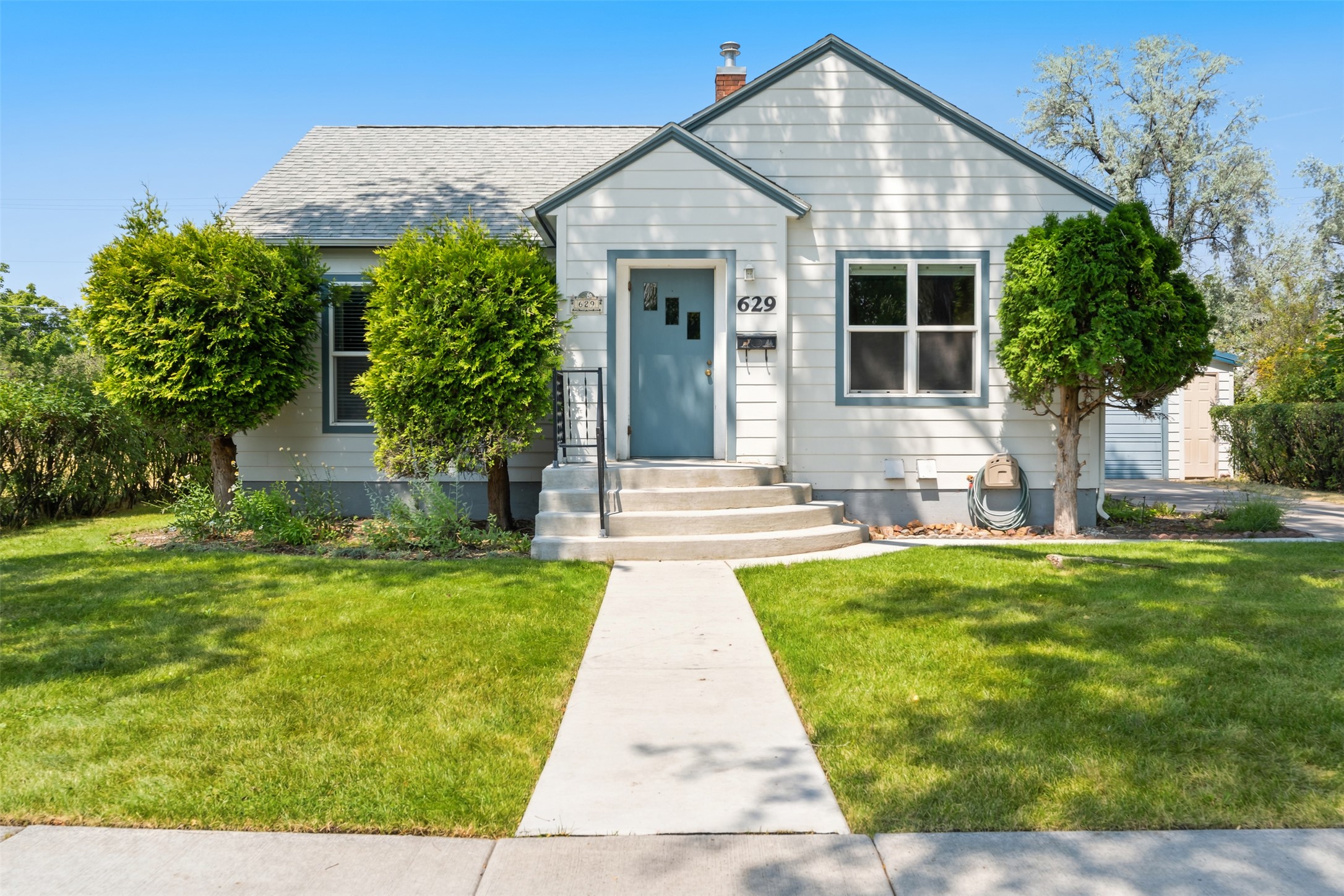 White-sided house with a blue front door, curved steps, and a walkway across the lawn.