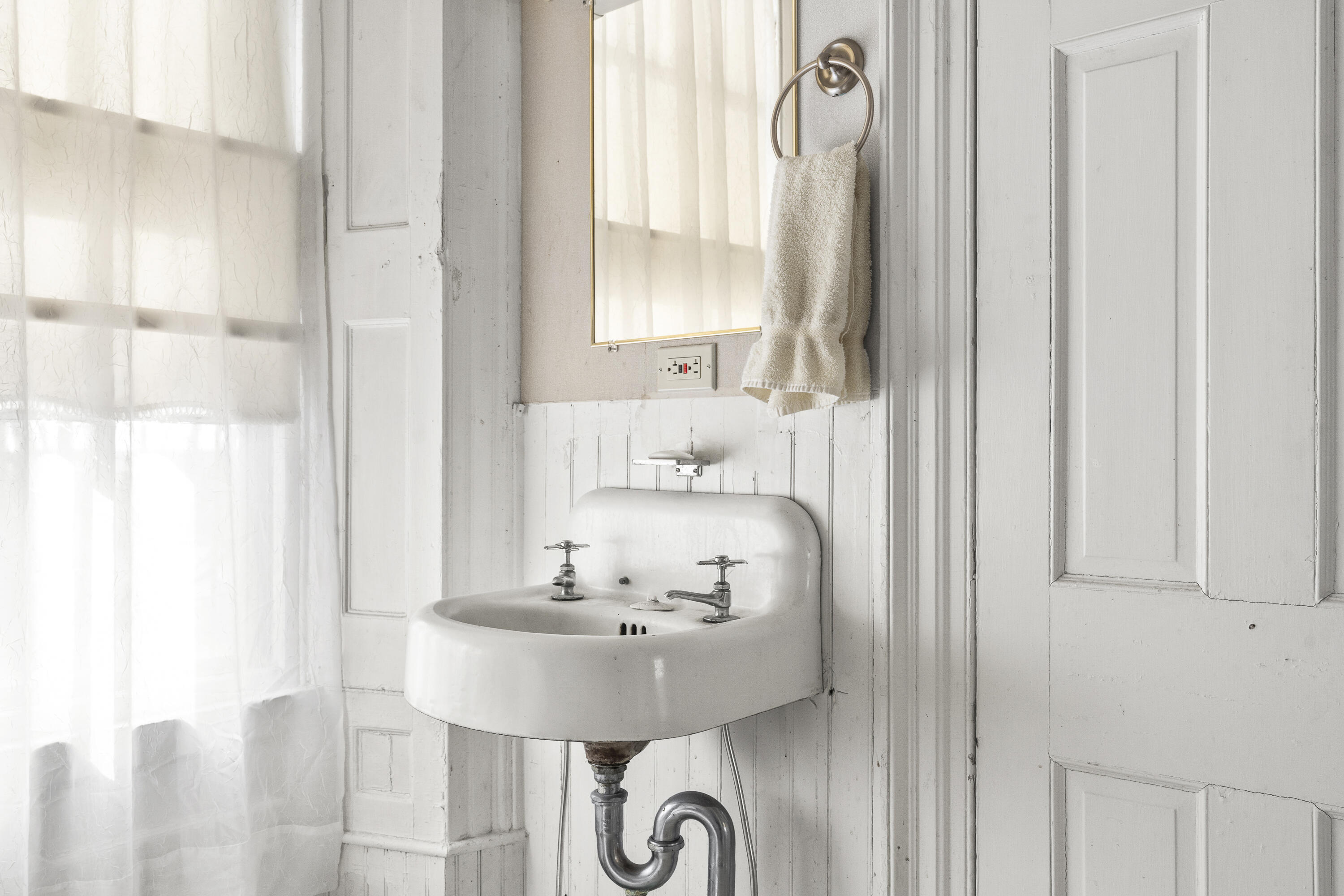 Bathroom with a vintage wall-mounted sink, exposed plumbing, and white paneled walls.