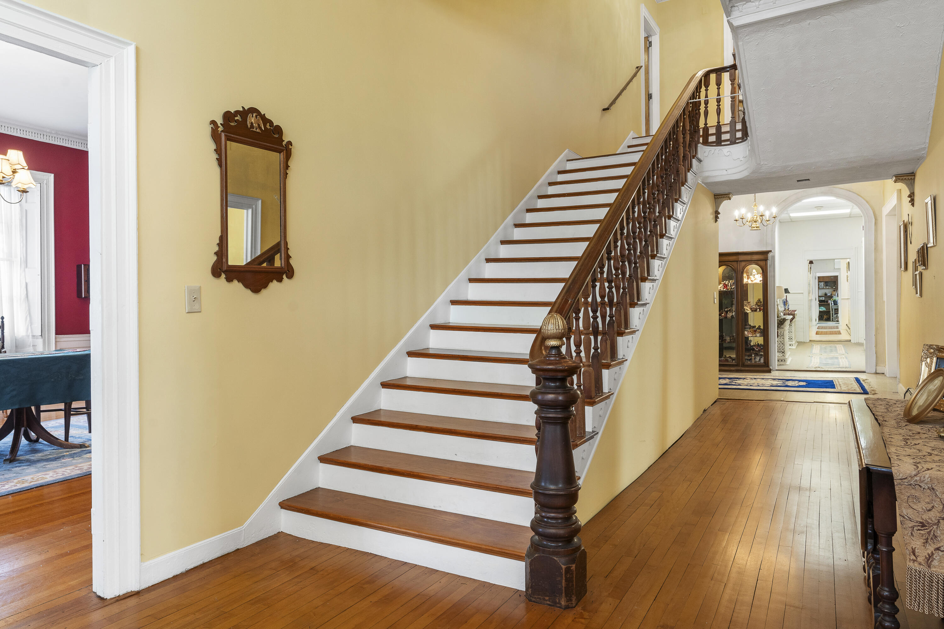 Grand foyer with a polished wood staircase, carved banister, and adjoining hallway.