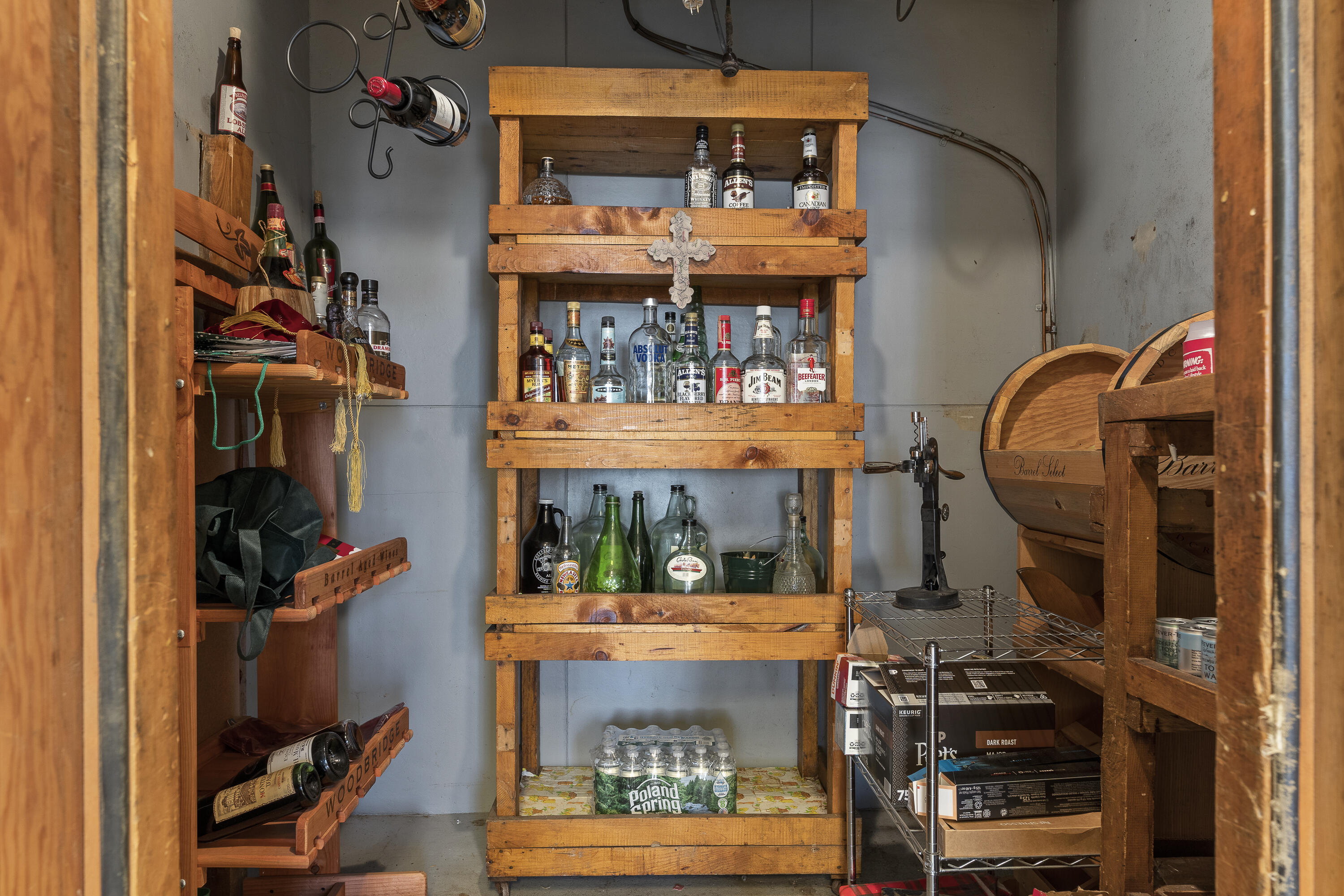 Storage room with rustic wooden shelves stocked with bottles and wooden beverage barrels.