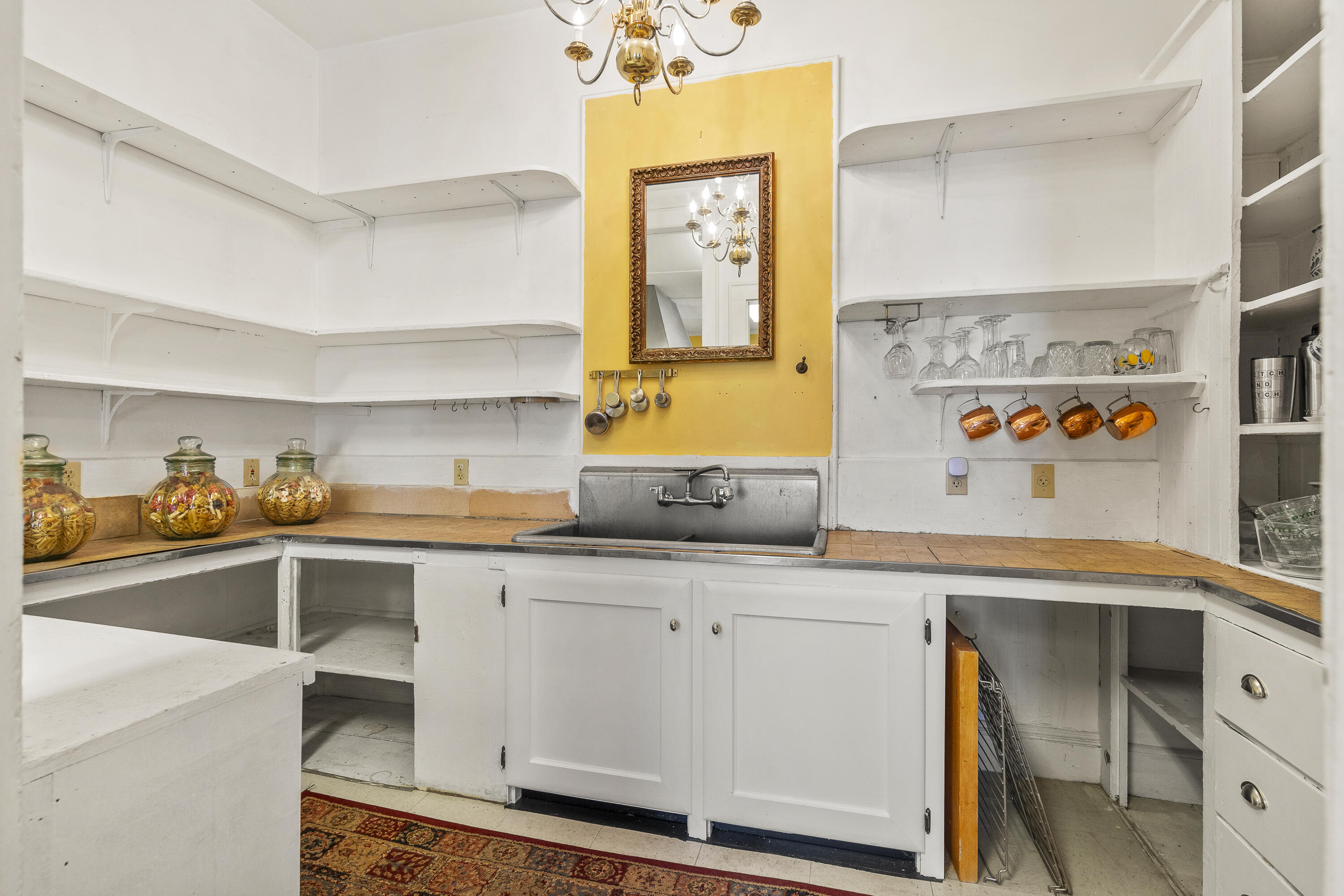 Kitchen with white built-in shelving, a deep sink, and a yellow wall with an ornate mirror.