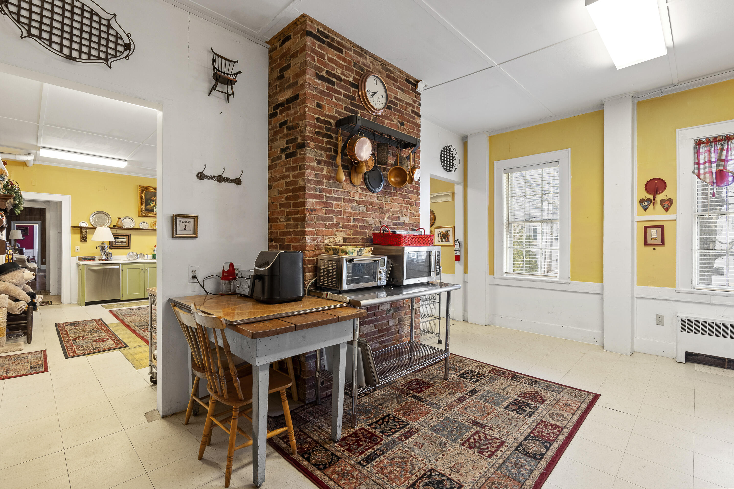 Kitchen with a brick chimney, hanging copper pans, yellow walls, and patterned rugs.