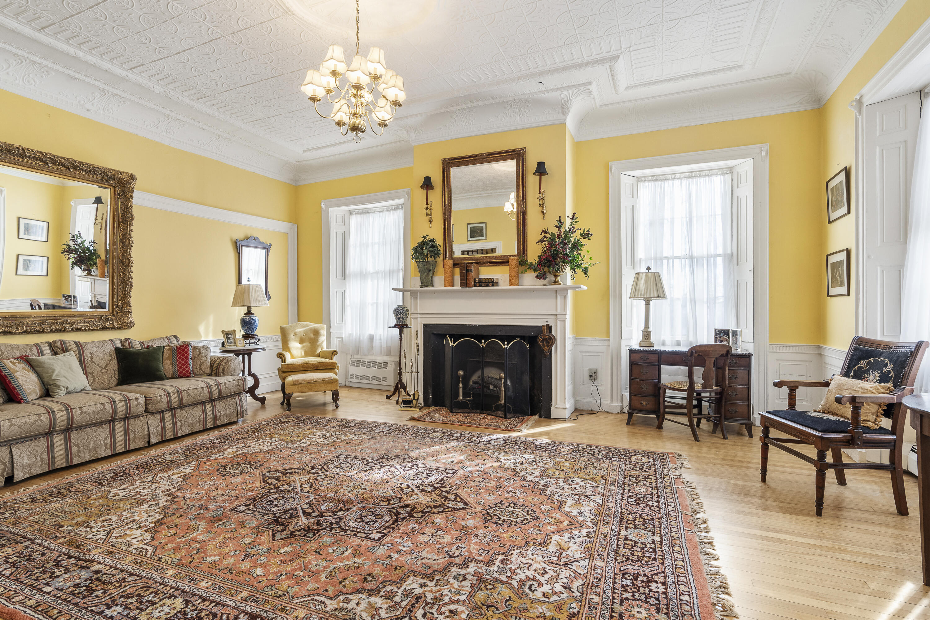 Living room with a fireplace, ornate pressed-tin ceiling, yellow walls, and a large patterned rug.