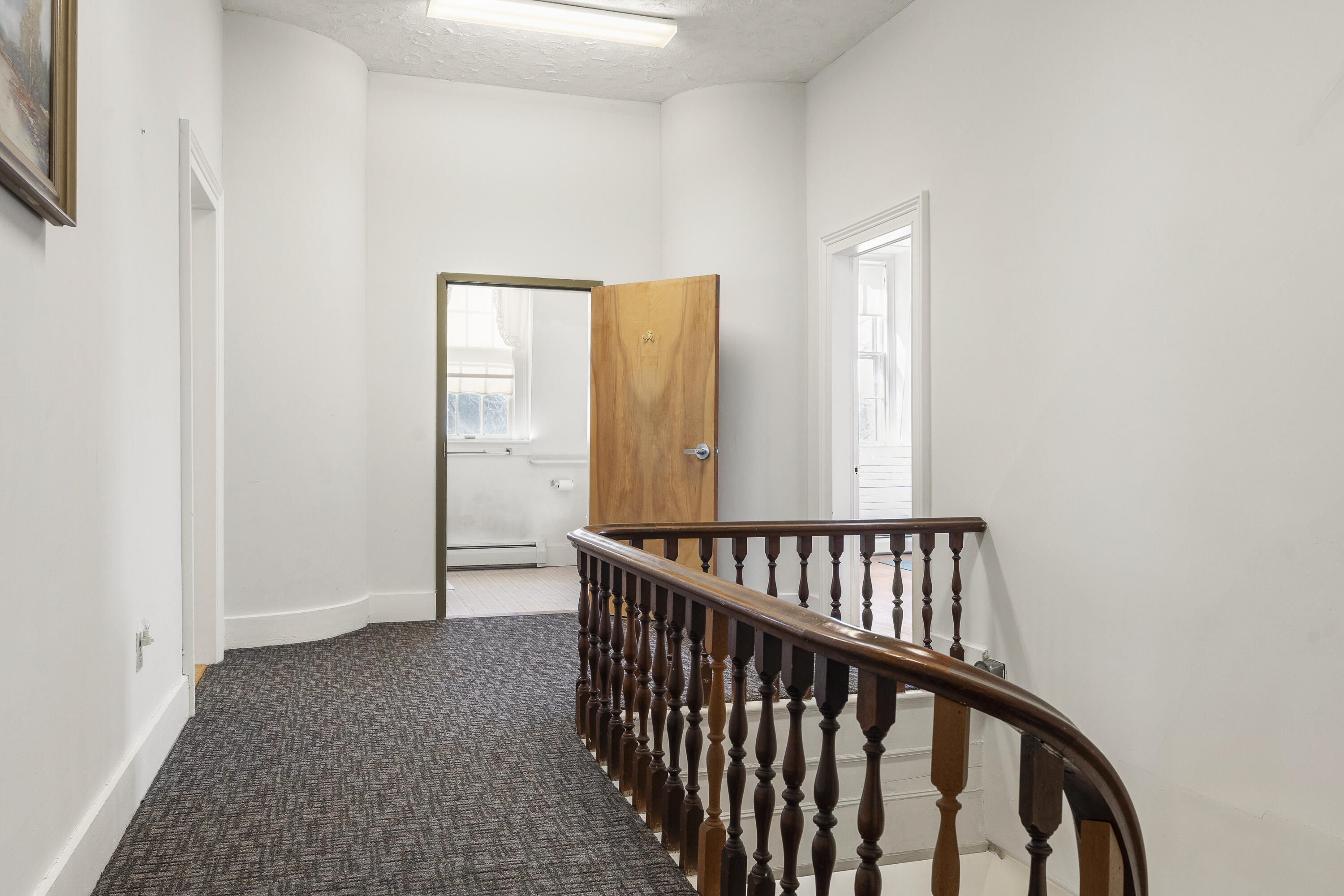 Upstairs landing with a curved dark wood railing, patterned carpet, and an open bathroom doorway.