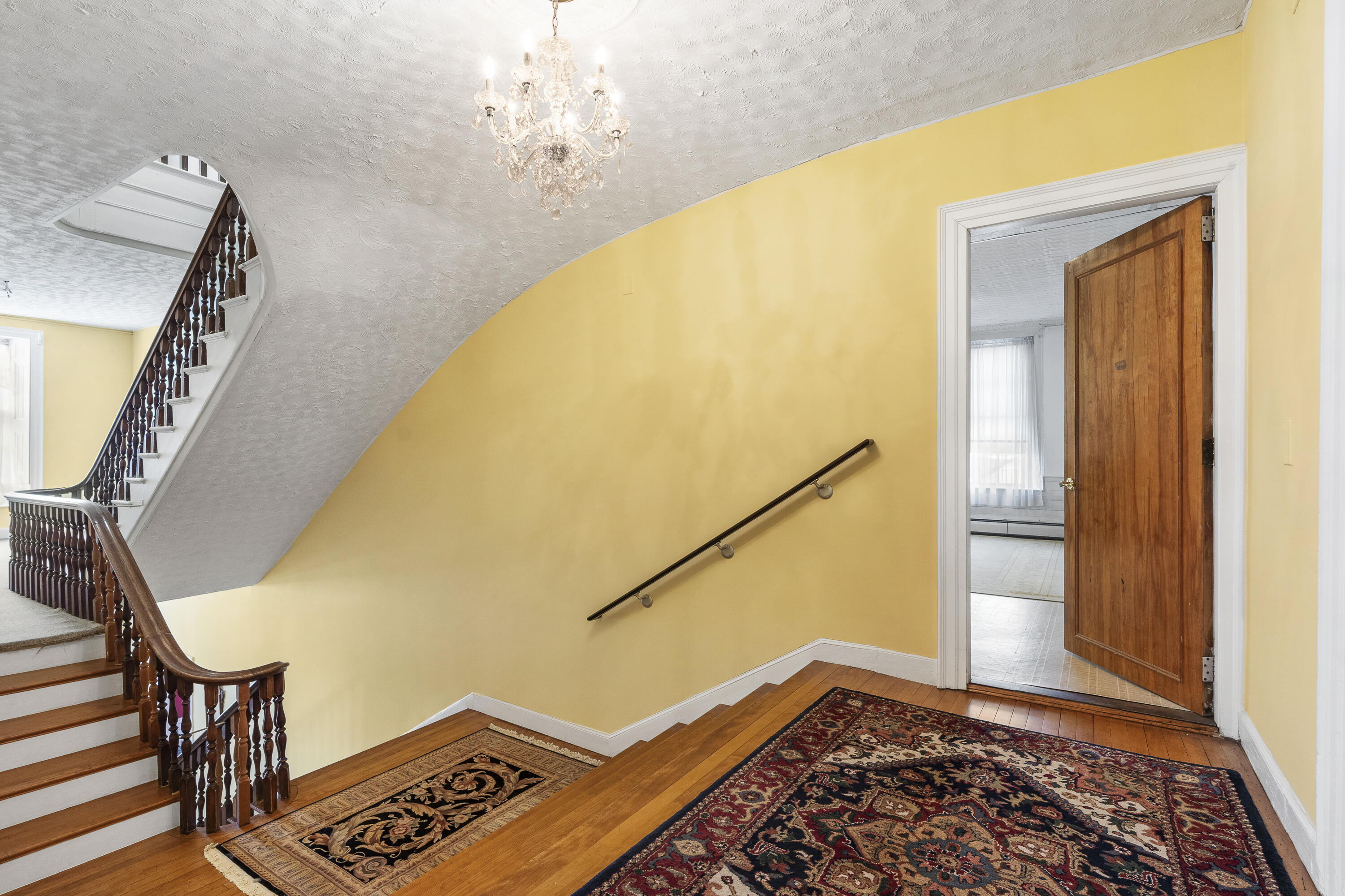 Foyer with a curved staircase, dark wood banister, crystal chandelier, and patterned rugs.