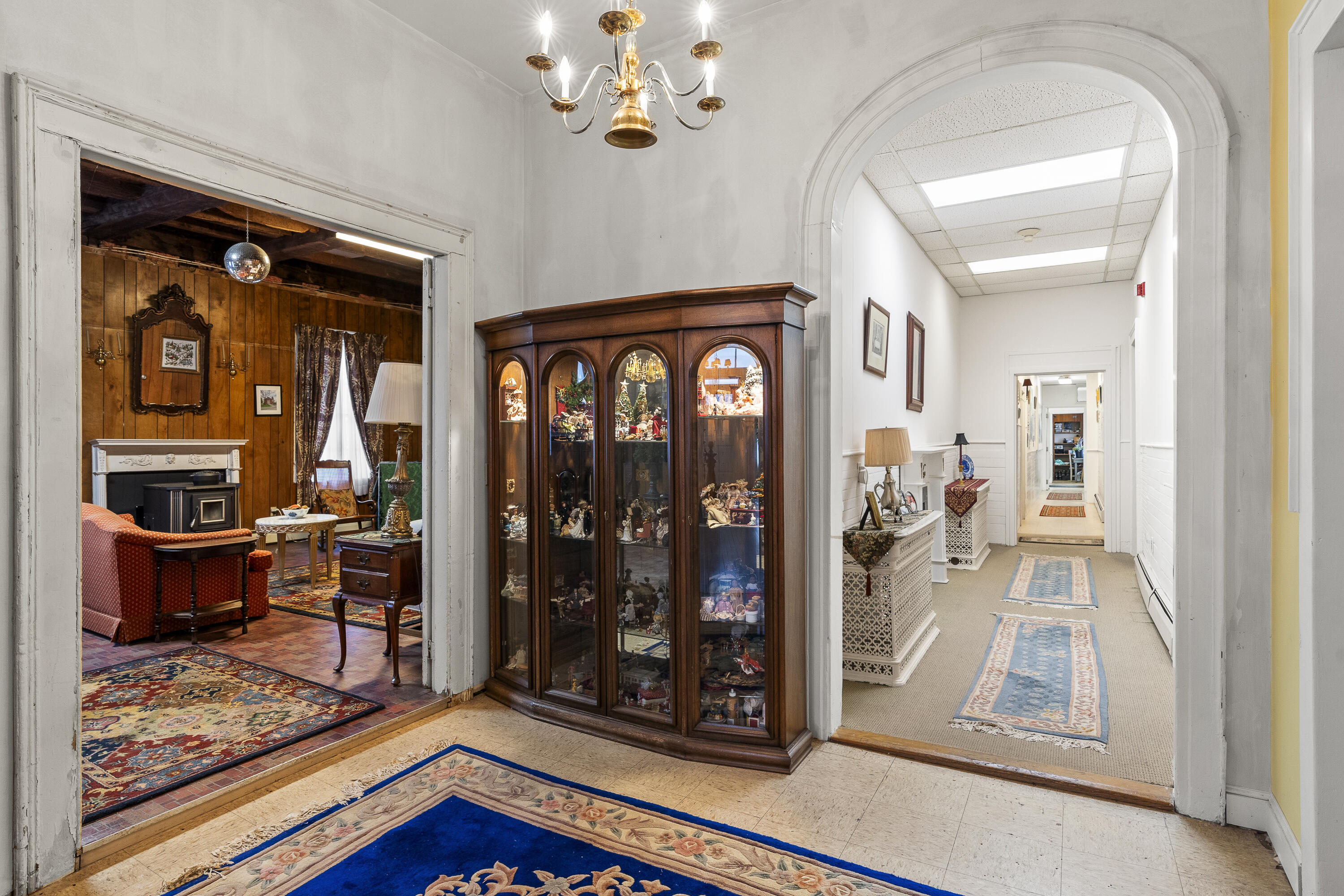 Furnished hallway with an arched opening, collectible display cabinet, and adjoining wood-paneled living room.