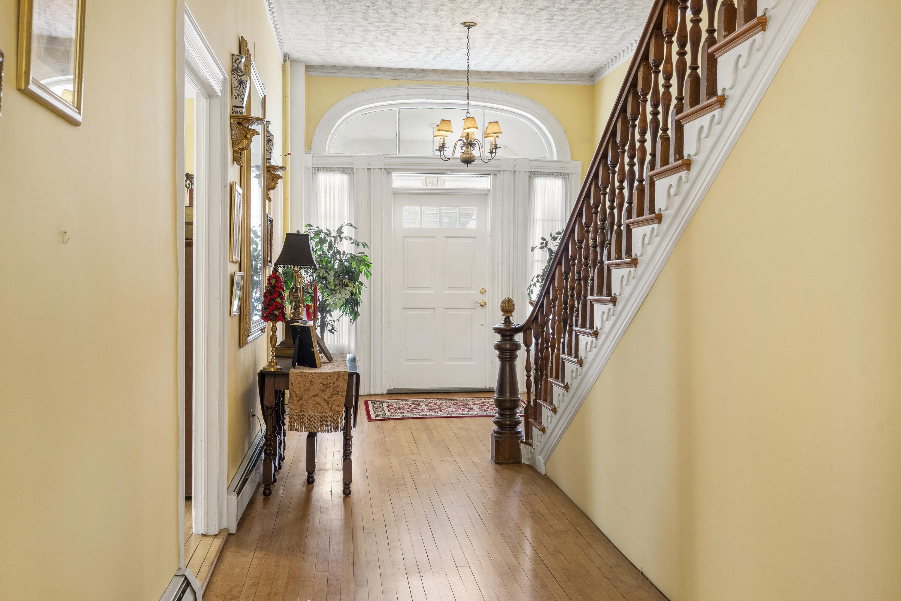 Entry hall with hardwood floors, an arched transom over the front door, and a dark wood staircase.