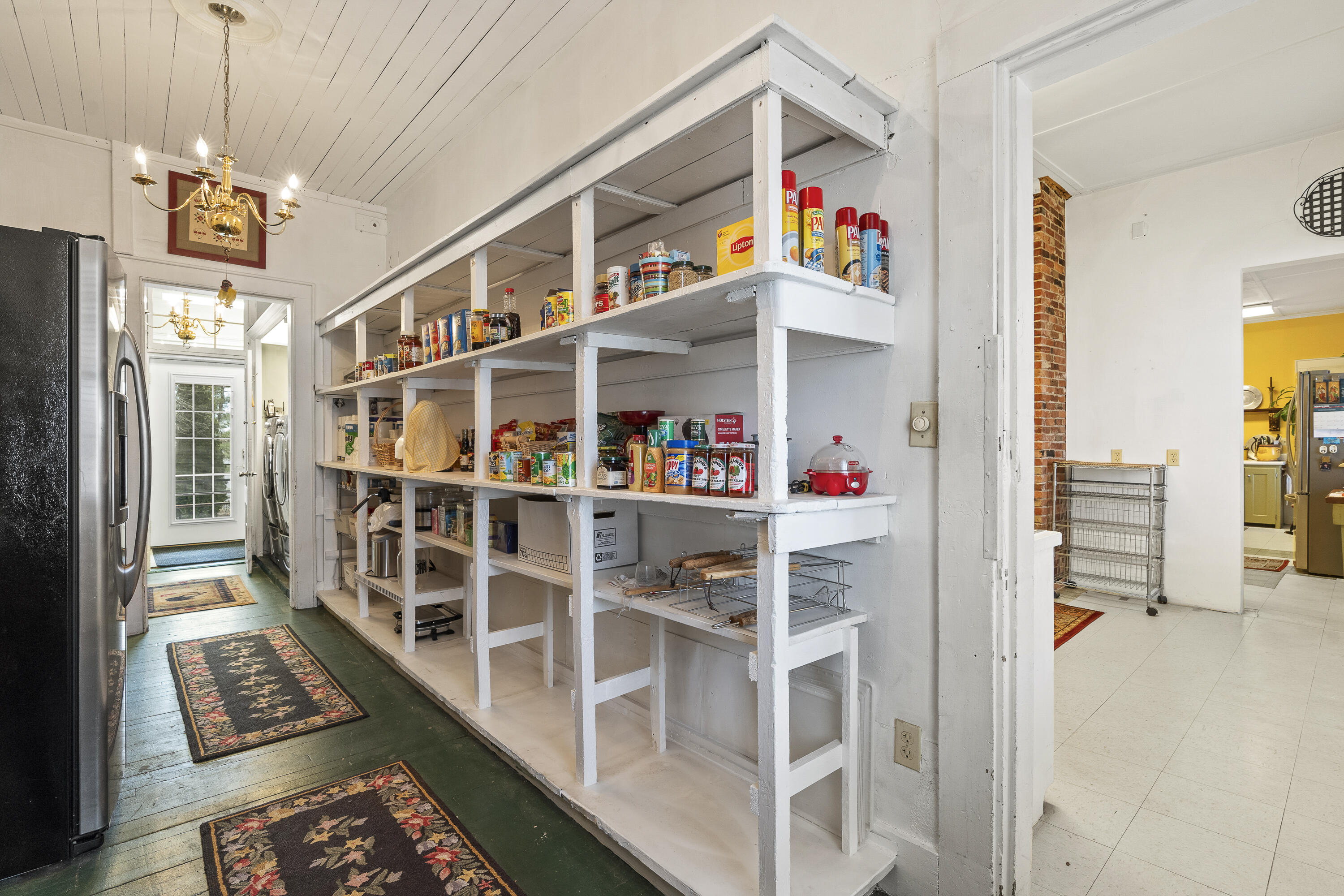 Pantry with stocked white open shelving beside a black refrigerator and green-painted wood floor.