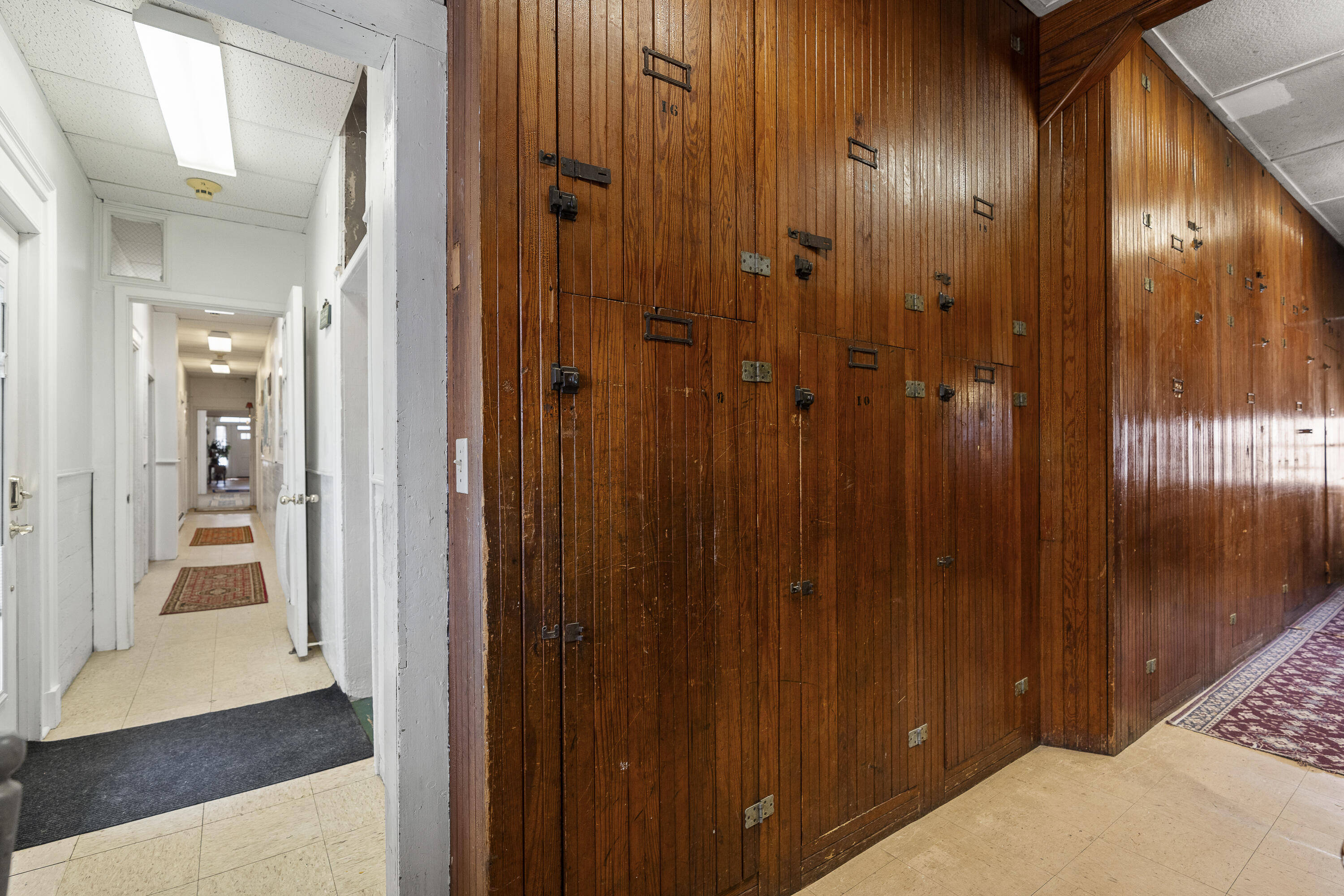 Hallway lined with dark wooden storage lockers beside a white corridor with patterned rugs.