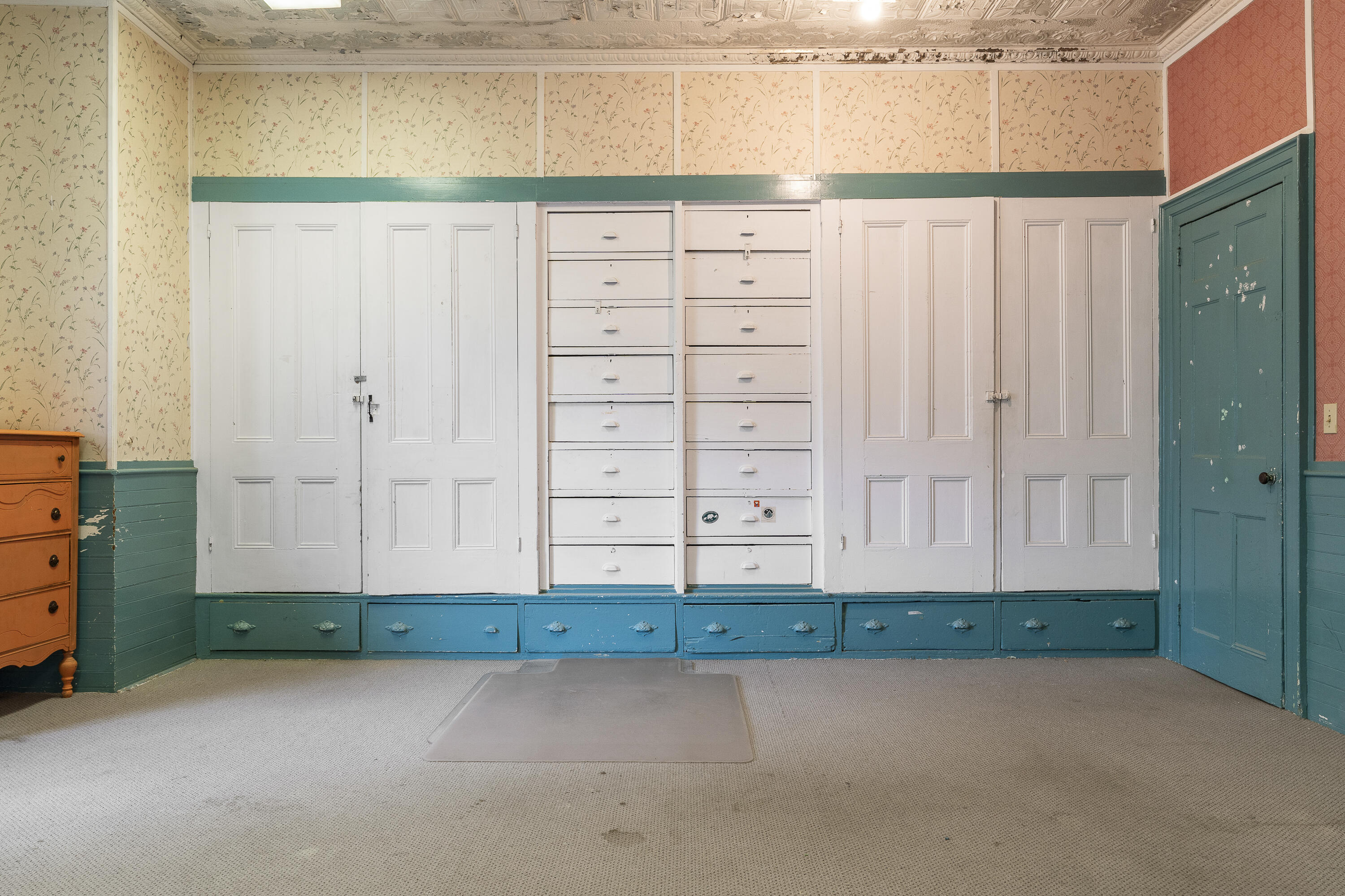 Room with built-in white cabinets and drawers, teal trim, floral wallpaper, and an ornate ceiling.
