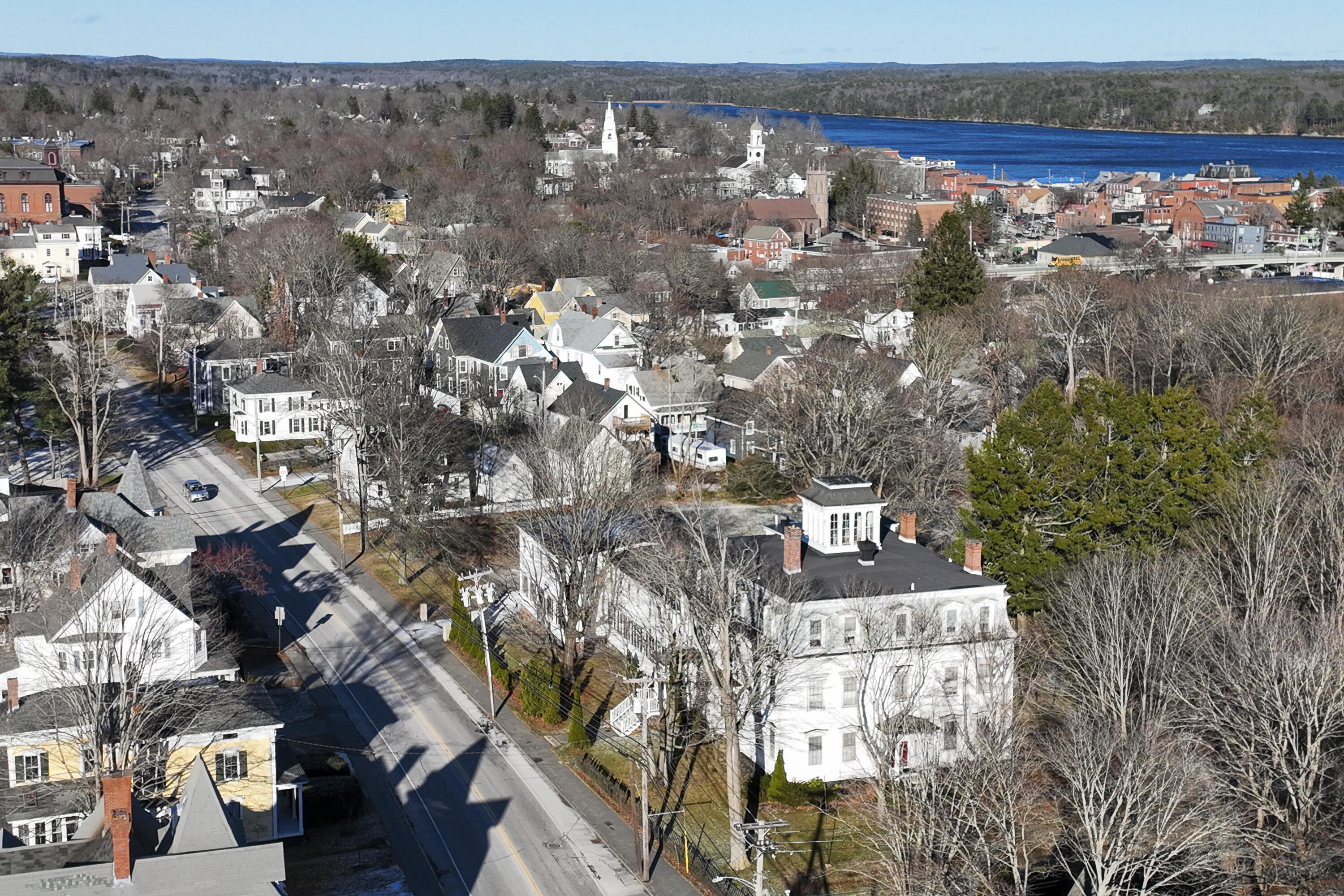 Aerial view of Bath homes, with a prominent white house in the foreground and the river beyond downtown.