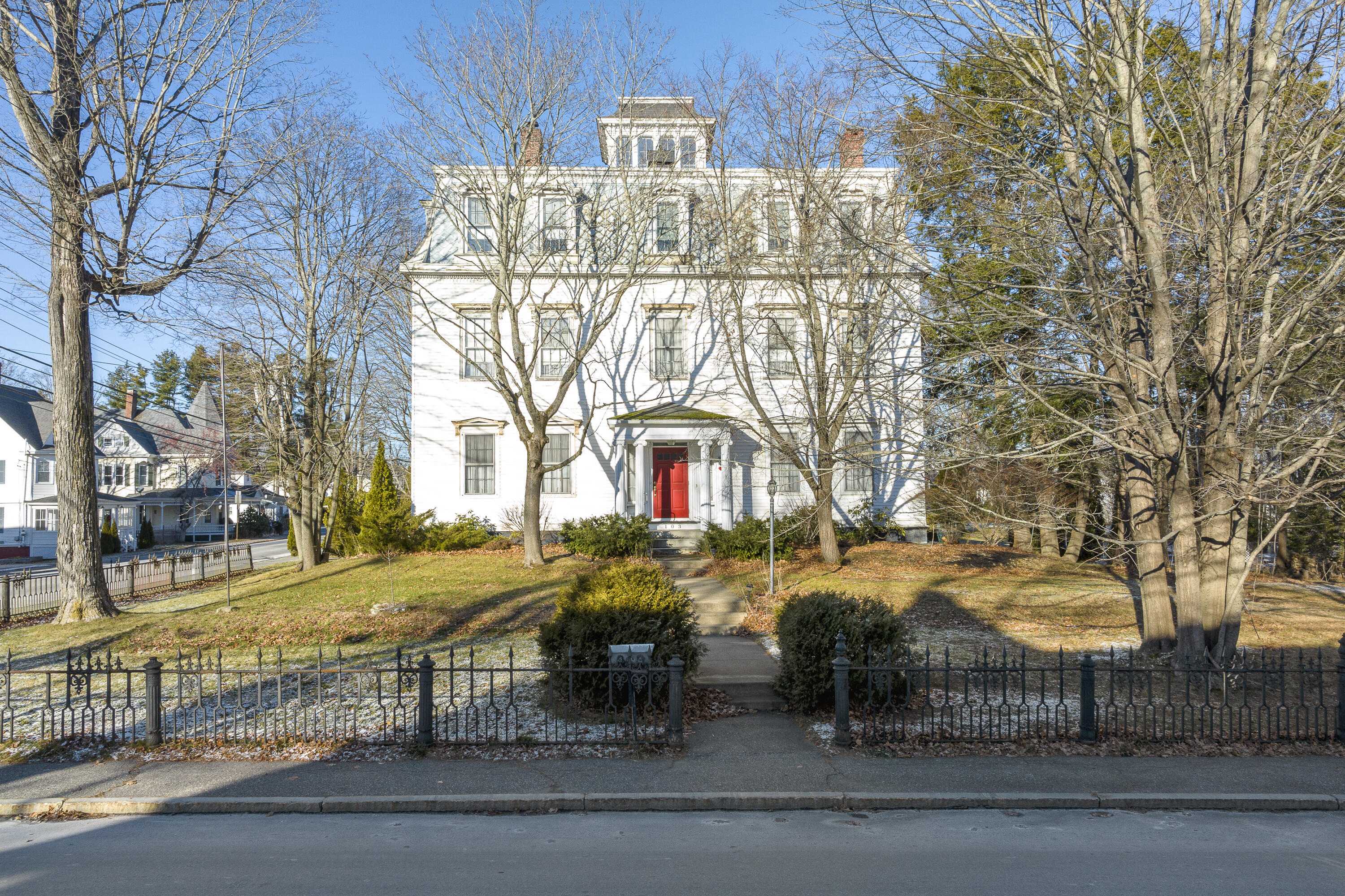 White multi-story home with a red front door behind an ornamental iron fence.