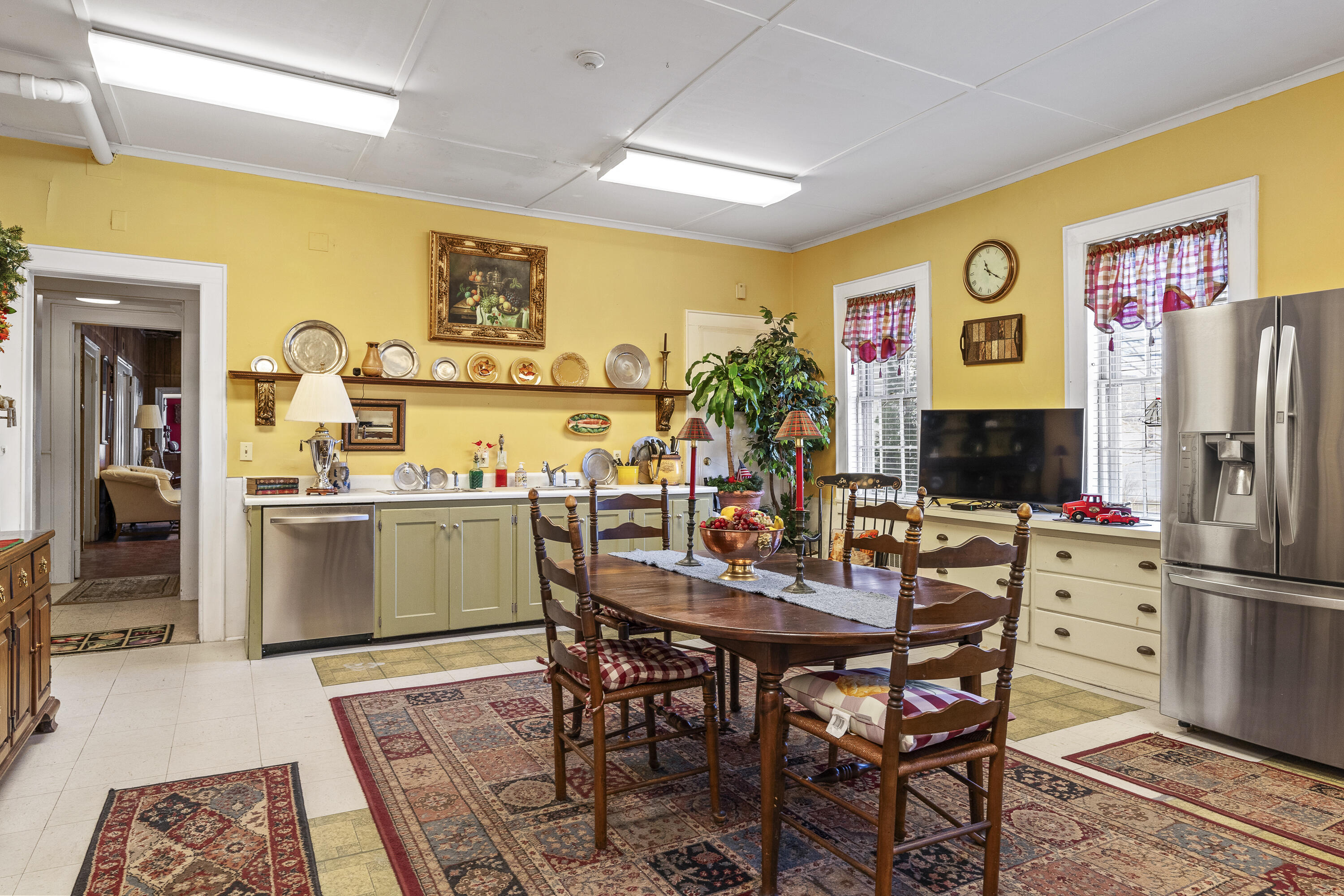 Kitchen and dining area with yellow walls, a wood table, stainless steel appliances, and patterned rugs.