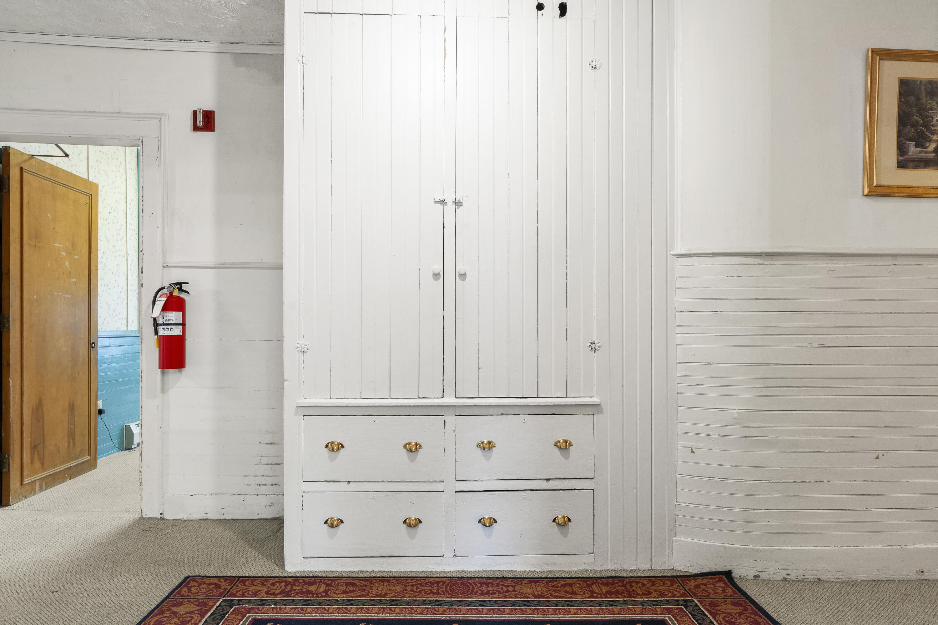 White built-in cupboard and drawers beside an open wooden doorway and patterned rug.