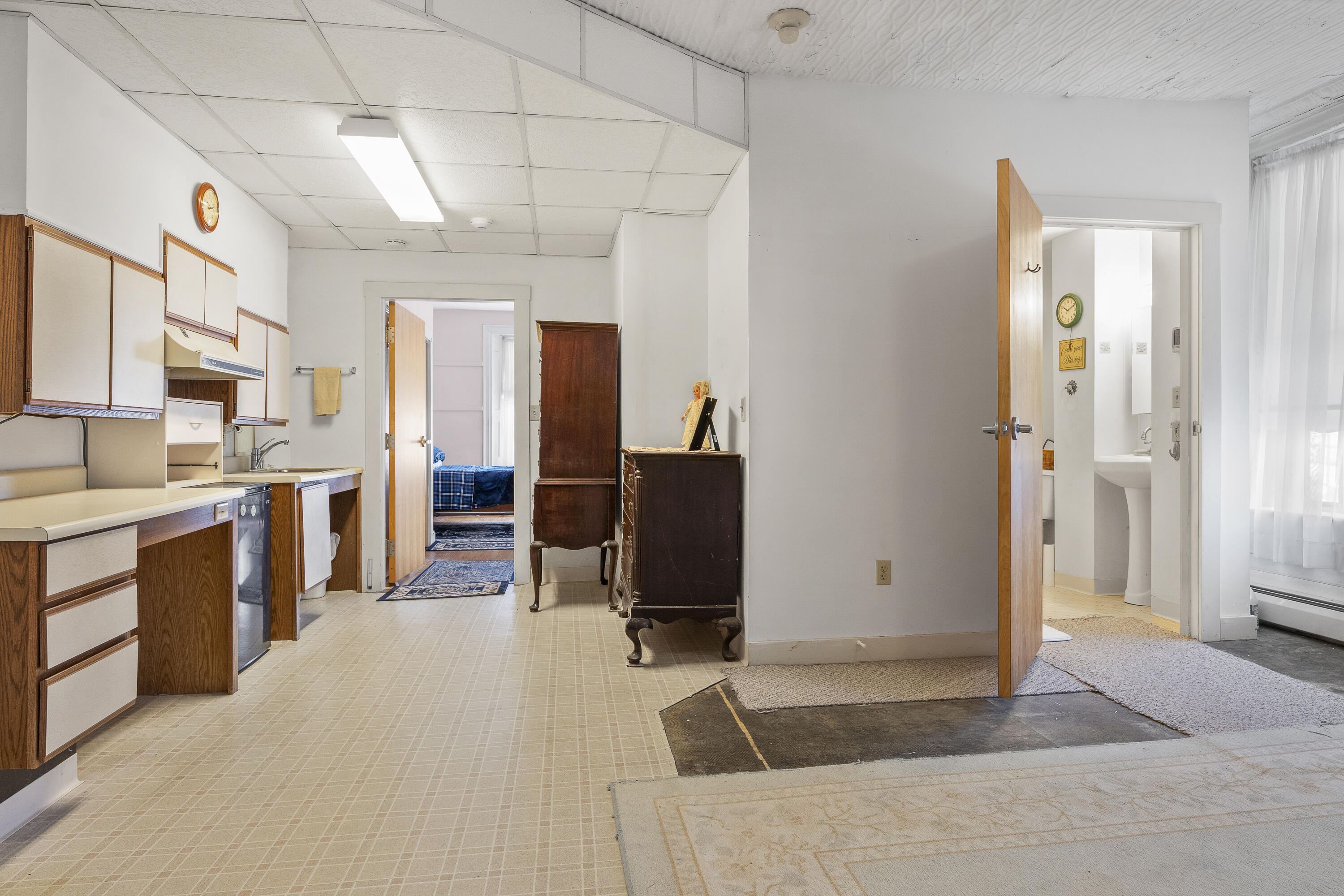 Kitchen with wood cabinets and compact refrigerator, opening to a bedroom and bathroom.