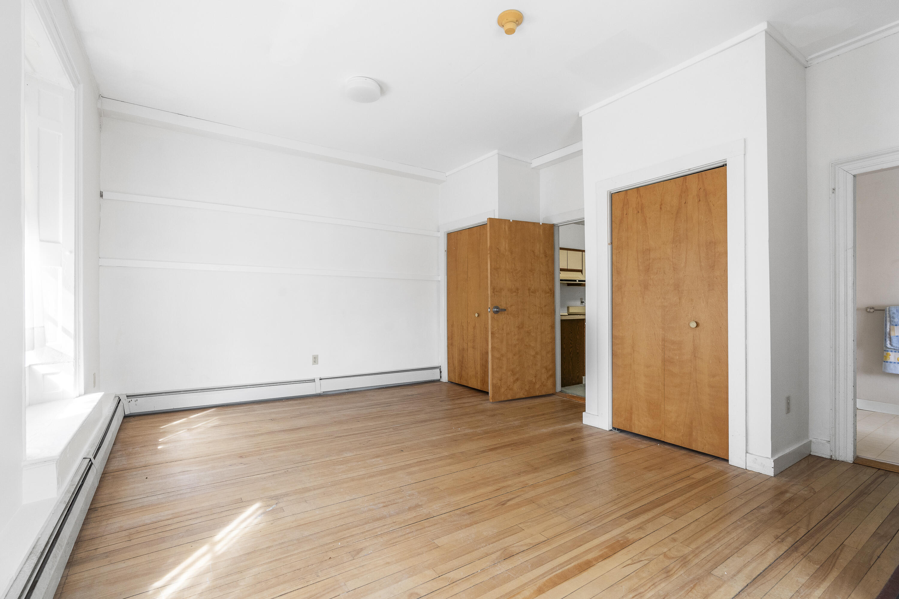 Empty room with hardwood floors, a large window, and wood closet doors.