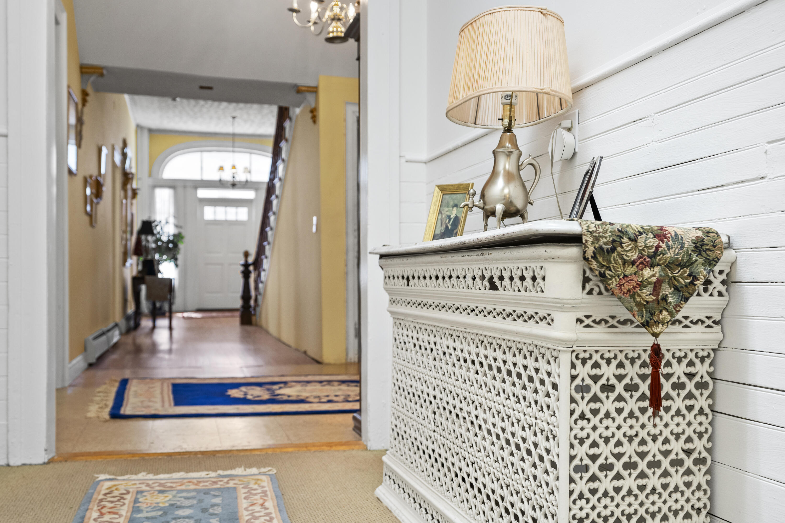 Entry hall with an ornate radiator cover and brass lamp beside a staircase and arched front-door window.