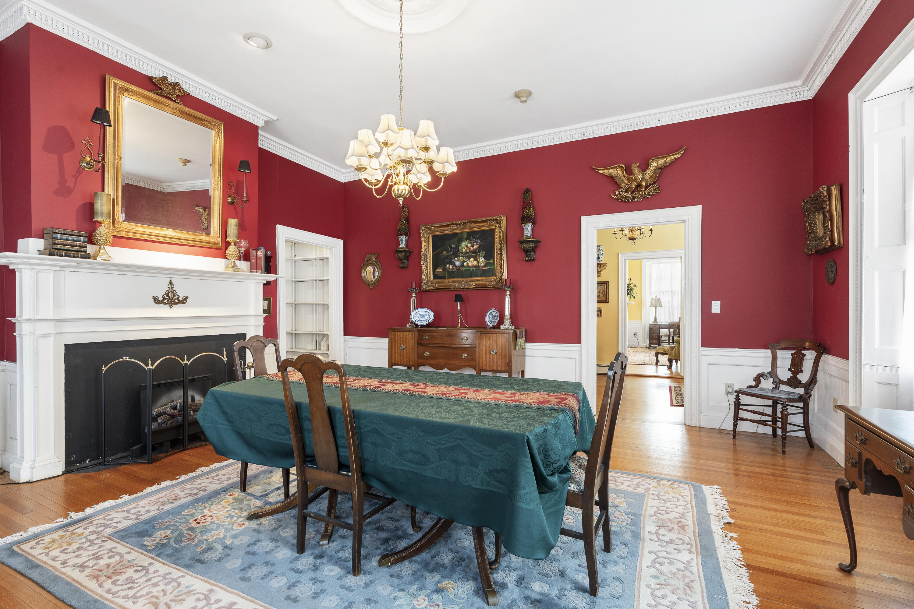 Formal dining room with crimson walls, ornate fireplace, chandelier, and teal-covered table.