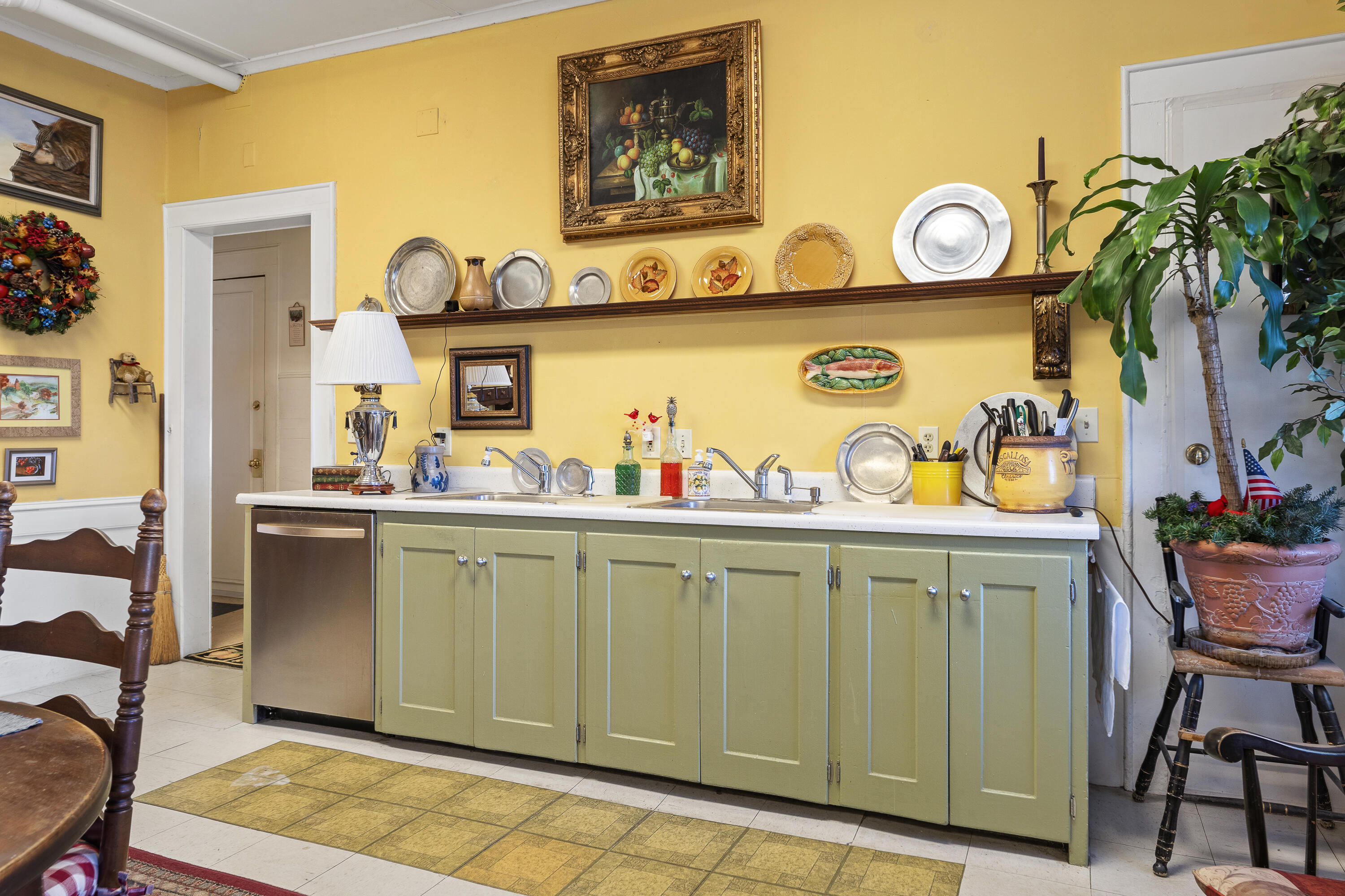 Kitchen with pale green cabinets, yellow walls, decorative plates, and a large potted plant.