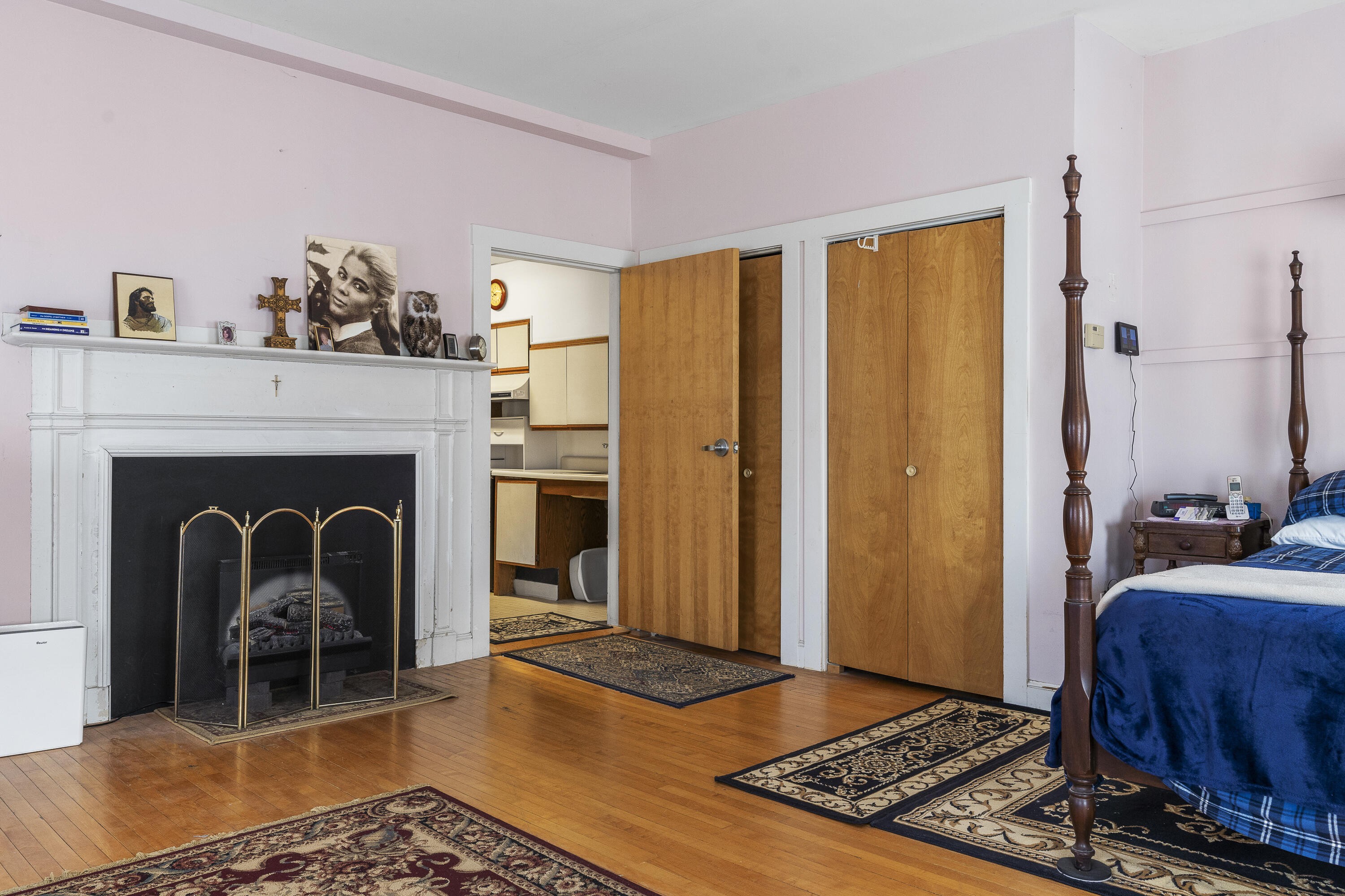 Bedroom with a white fireplace, hardwood floors, patterned rugs, and a dark wood four-poster bed.
