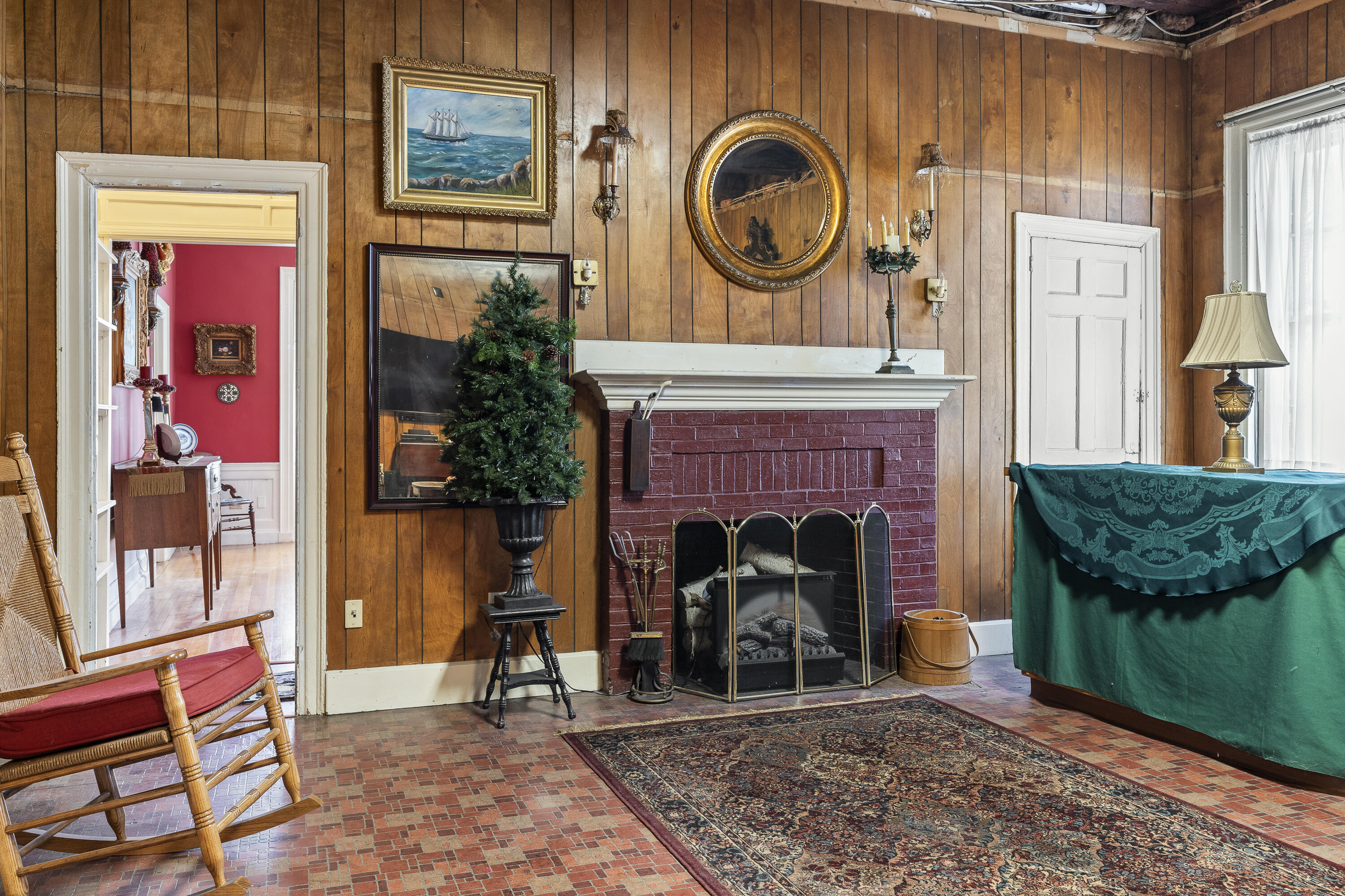 Living room with wood-paneled walls, a red brick fireplace, and a small Christmas tree beside the mantel.