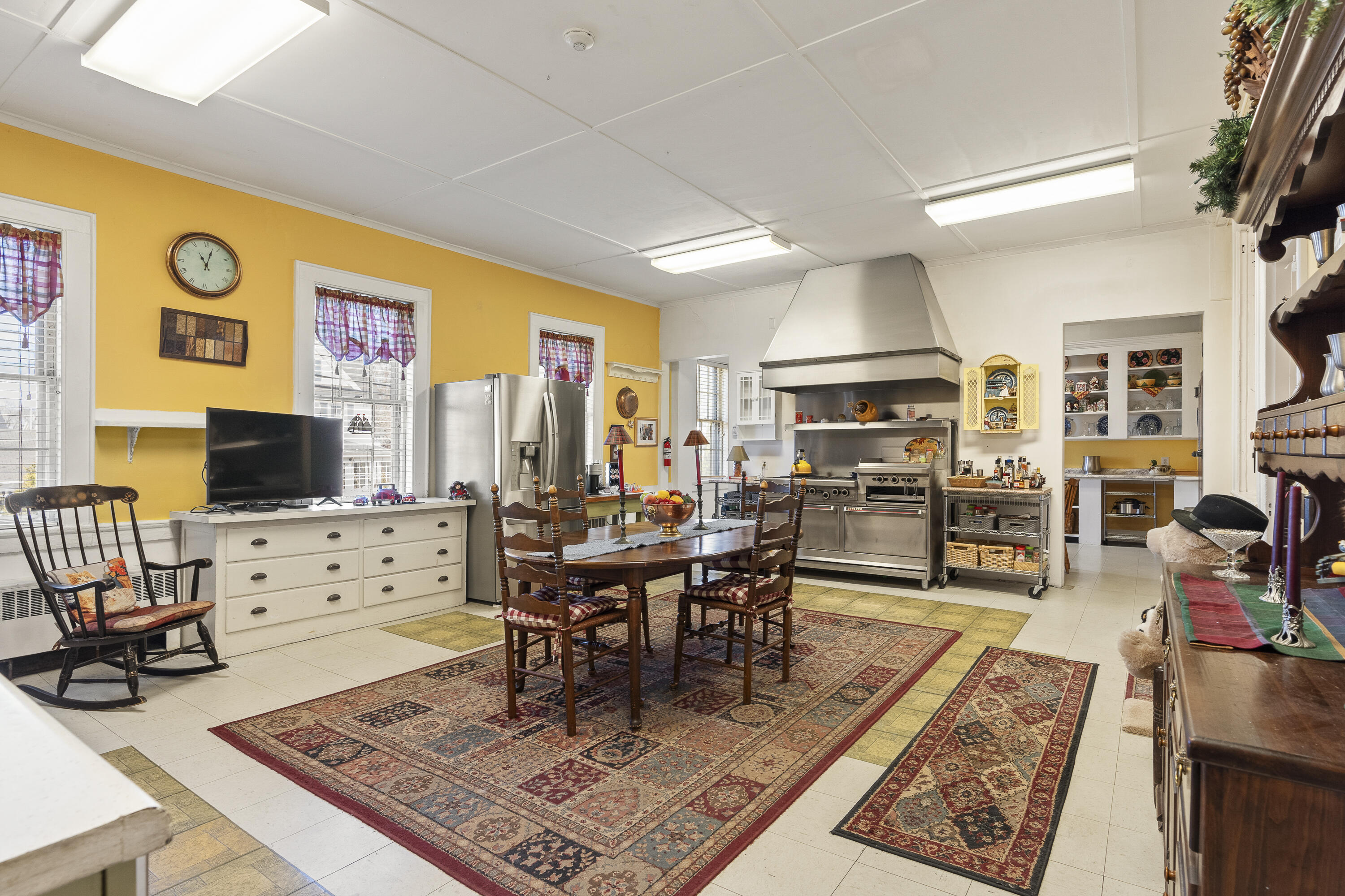Kitchen with yellow walls, stainless-steel range and hood, and a wooden dining table on patterned rugs.