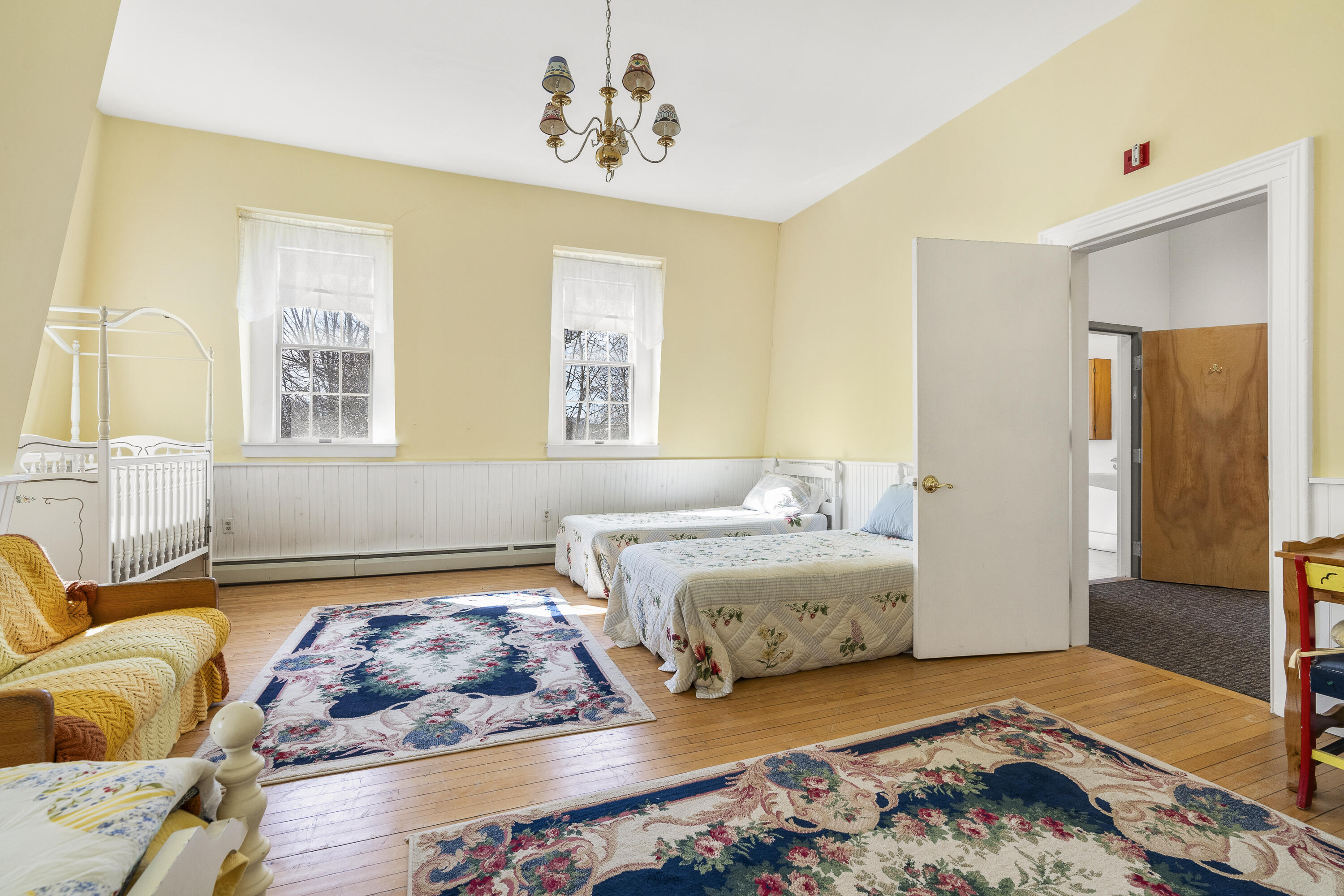 Bedroom with two beds, yellow walls, hardwood floors, and floral rugs.