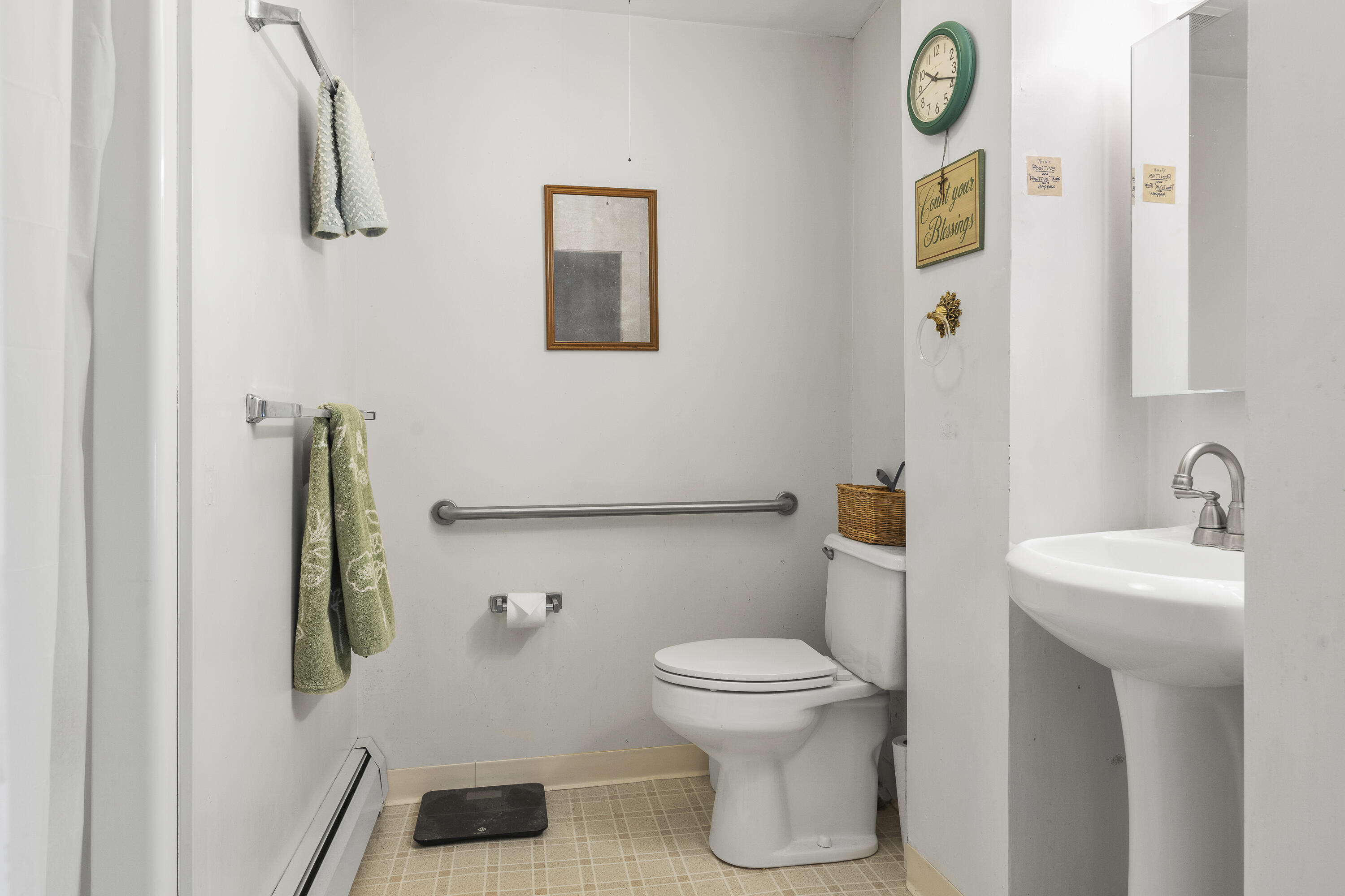 Bathroom with a toilet, pedestal sink, grab bars, and green towels.