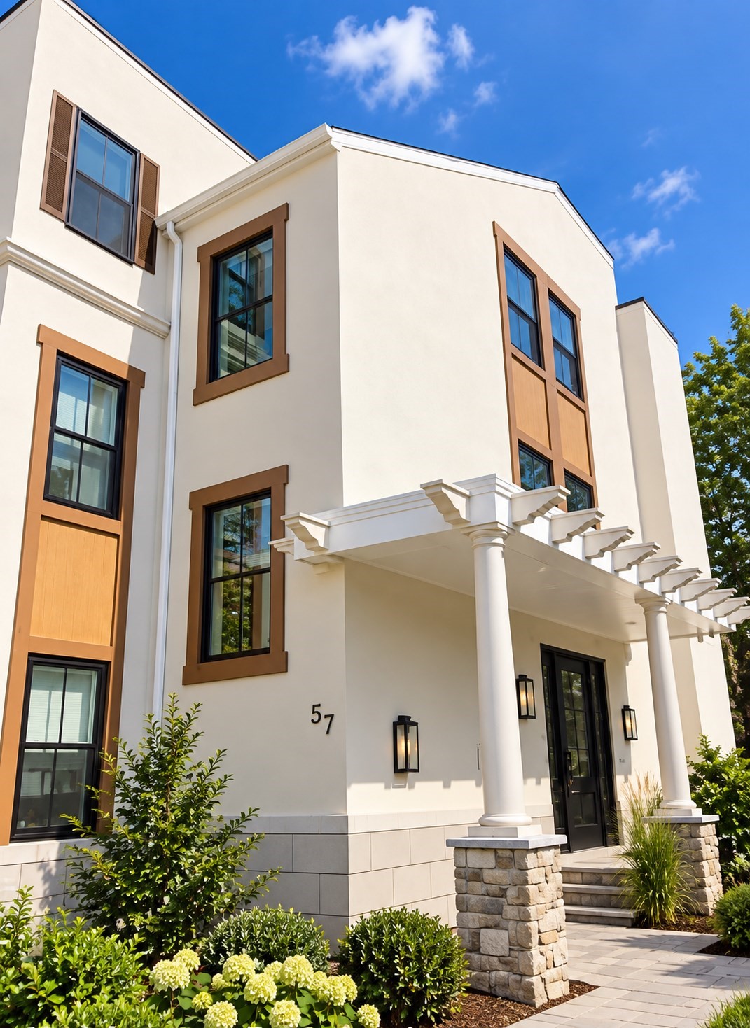White multi-story home with brown-trimmed windows, a columned portico, and landscaped entrance.