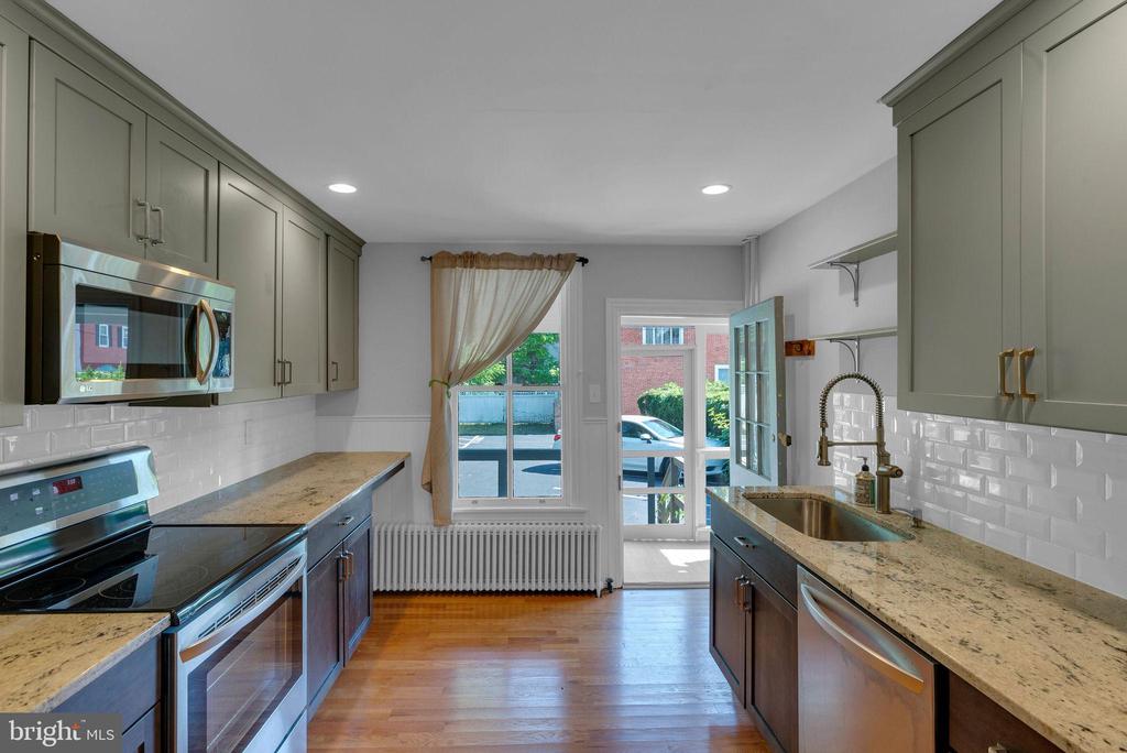 Kitchen with granite counters, subway tile, stainless appliances, and an open glass door.