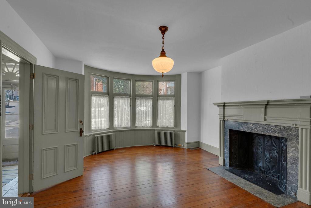 Vacant living room with bay windows, hardwood floors, and a large fireplace.