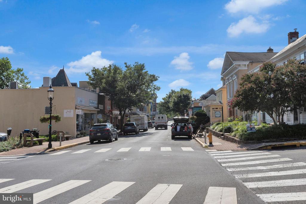 Town-center street with storefronts, parked cars, and crosswalks at an intersection.