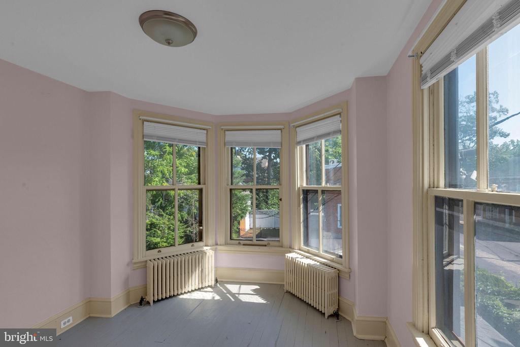 Vacant pink room with bay windows, tall side windows, white radiators, and a gray floor.