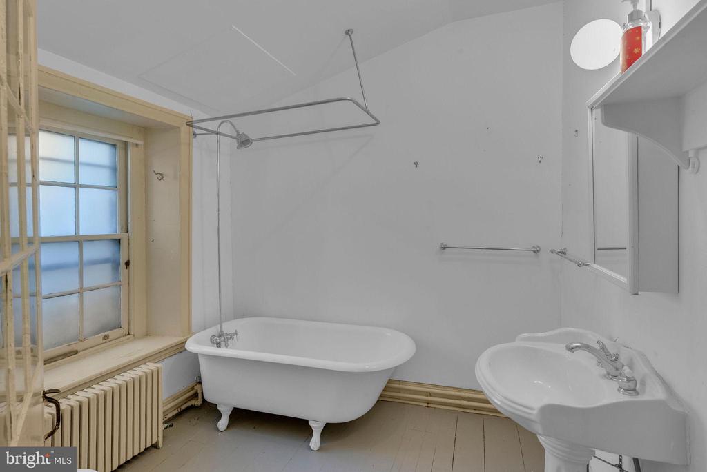 Bathroom with a claw-foot tub beneath a frosted-paned window and a pedestal sink.