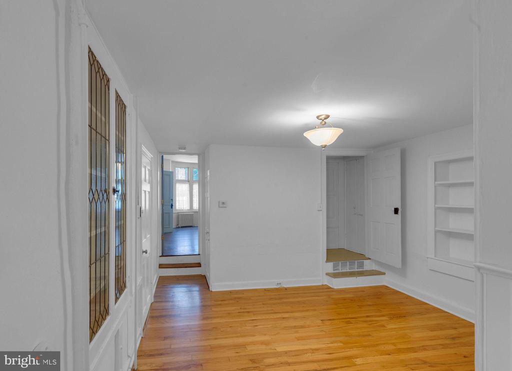 Vacant room with hardwood floors, built-in shelving, and a decorative glass-paneled door.