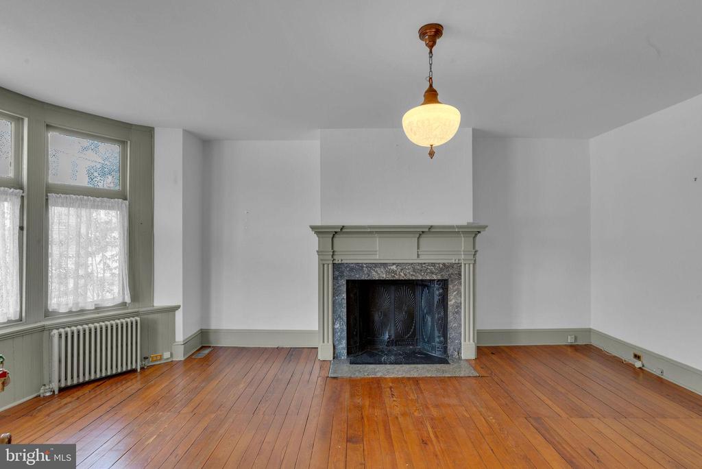 Vacant living room with polished hardwood floors, tall windows, and an ornate fireplace.
