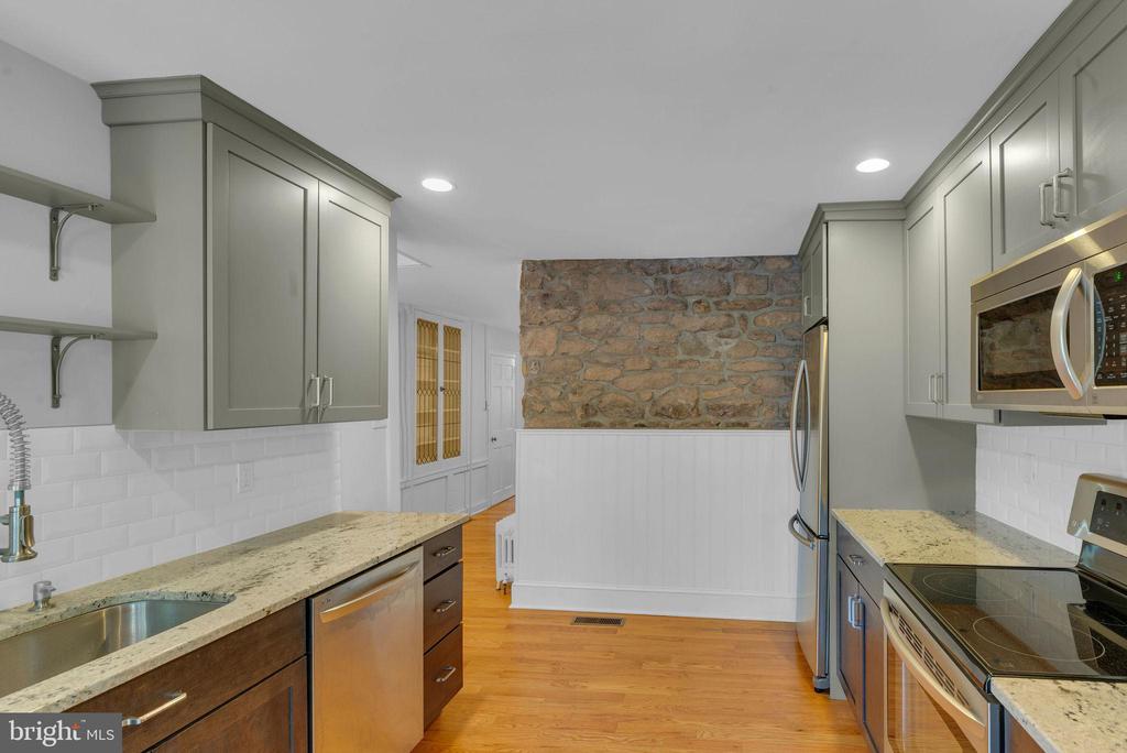 Kitchen with gray cabinets, stone countertops, stainless steel appliances, and an exposed stone wall.