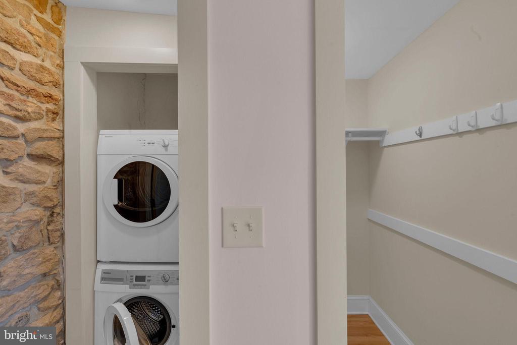 Laundry area with stacked washer and dryer beside a narrow closet and exposed stone wall.