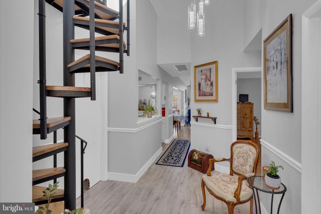 Entry hallway with a black spiral staircase, wood treads, patterned runner, and upholstered chair.