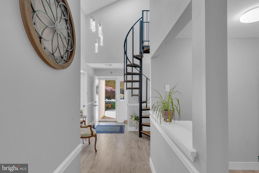 Entry foyer with a black spiral staircase, pale wood flooring, and an open front door.