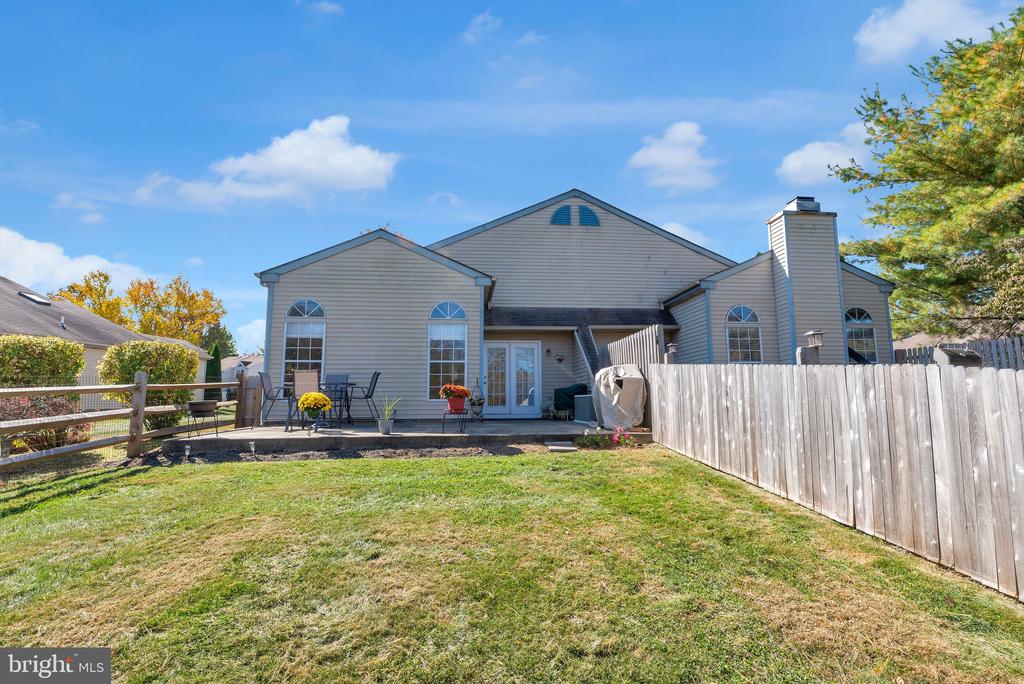 Rear of a gray-sided two-story home with a patio, lawn, and wooden privacy fence.