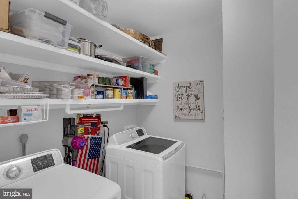 Laundry room with two top-loading machines and shelves stocked with household supplies.