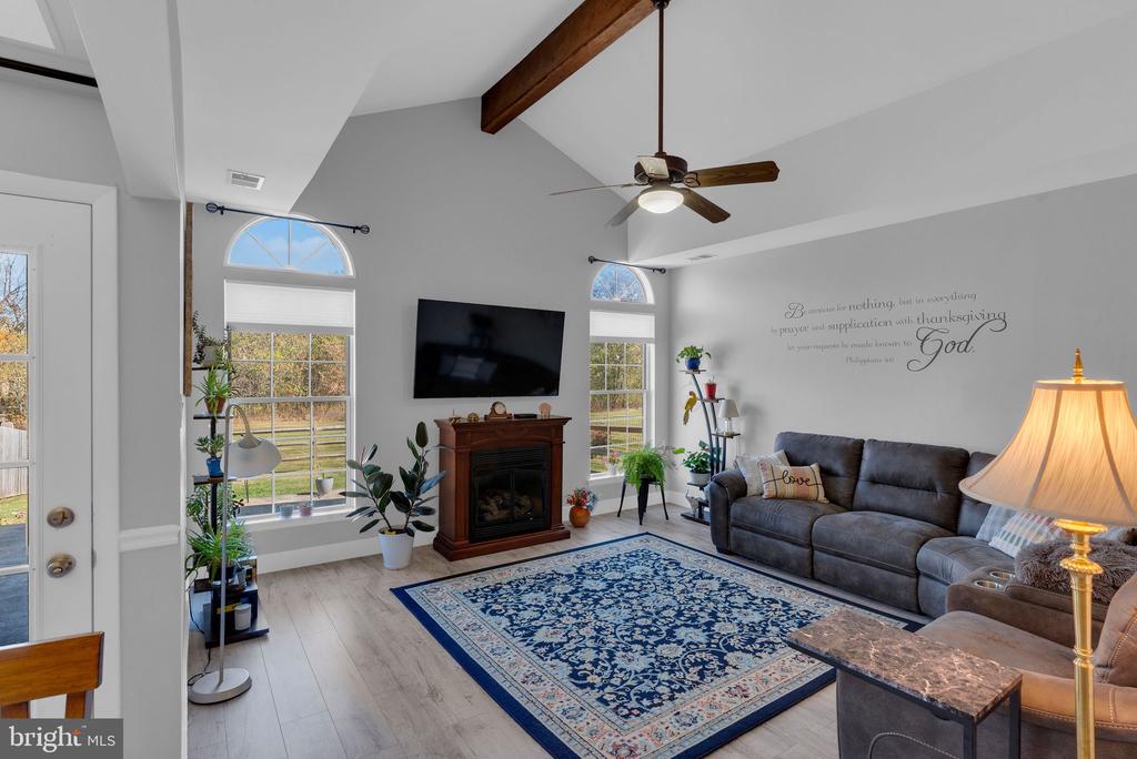 Living room with a vaulted ceiling, exposed beam, gray sofa, blue rug, and fireplace.