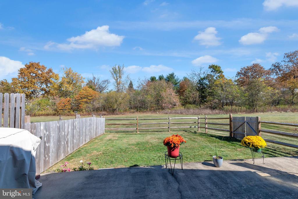 Back patio overlooking a fenced lawn and open field, with autumn trees beyond.