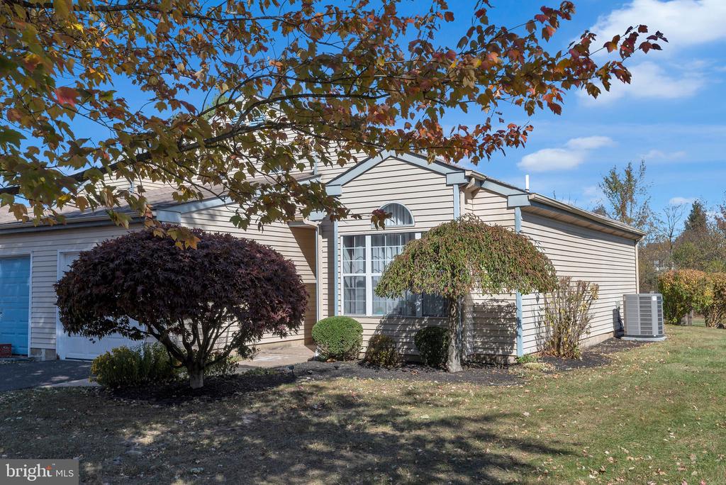 Single-story beige home with an attached garage, arched window, and autumn trees in the front yard.