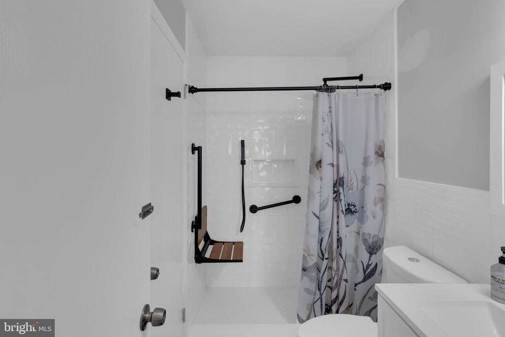 Bathroom with an accessible shower, grab bars, fold-down bench, and floral curtain.
