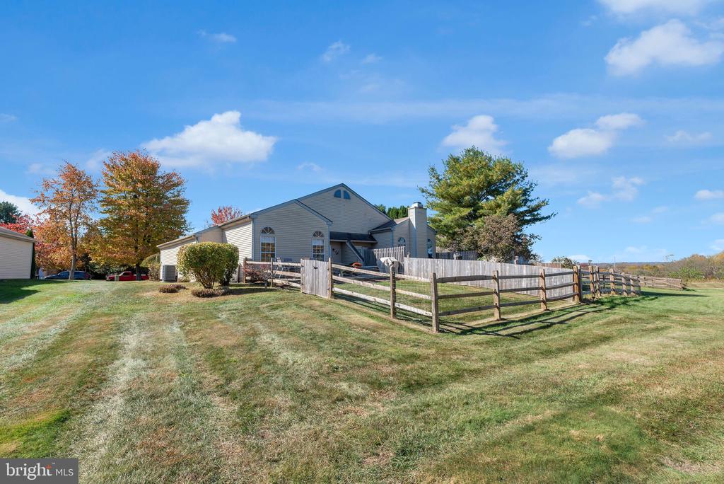 Gray-sided home with a fenced lawn, mature trees, and open fields beyond.